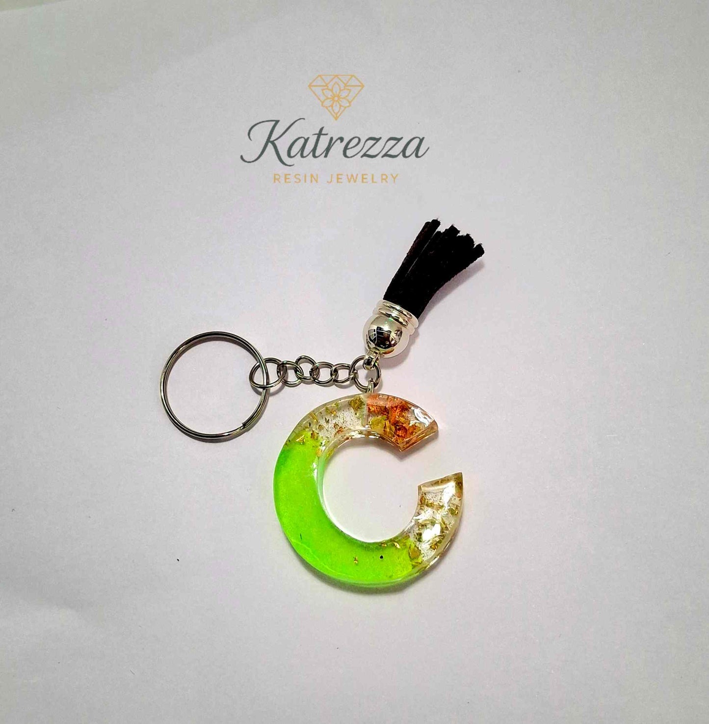 Bright green resin C keychain on silver chain with black tassel accessory.