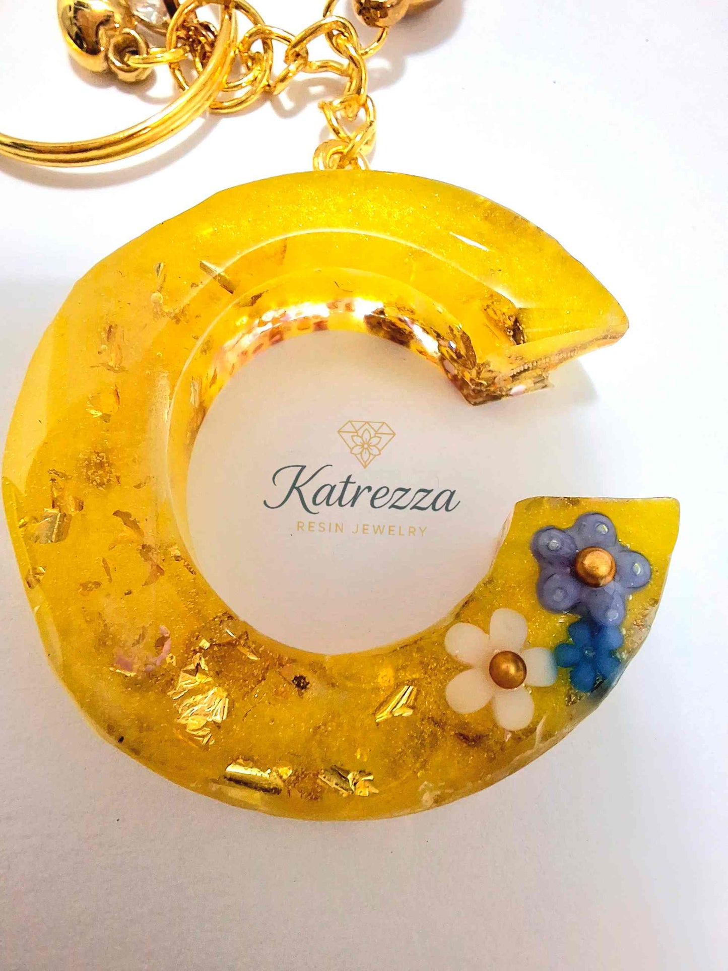 Close-up of handmade yellow resin C keychain with blue and white floral accents and shimmering gold details.