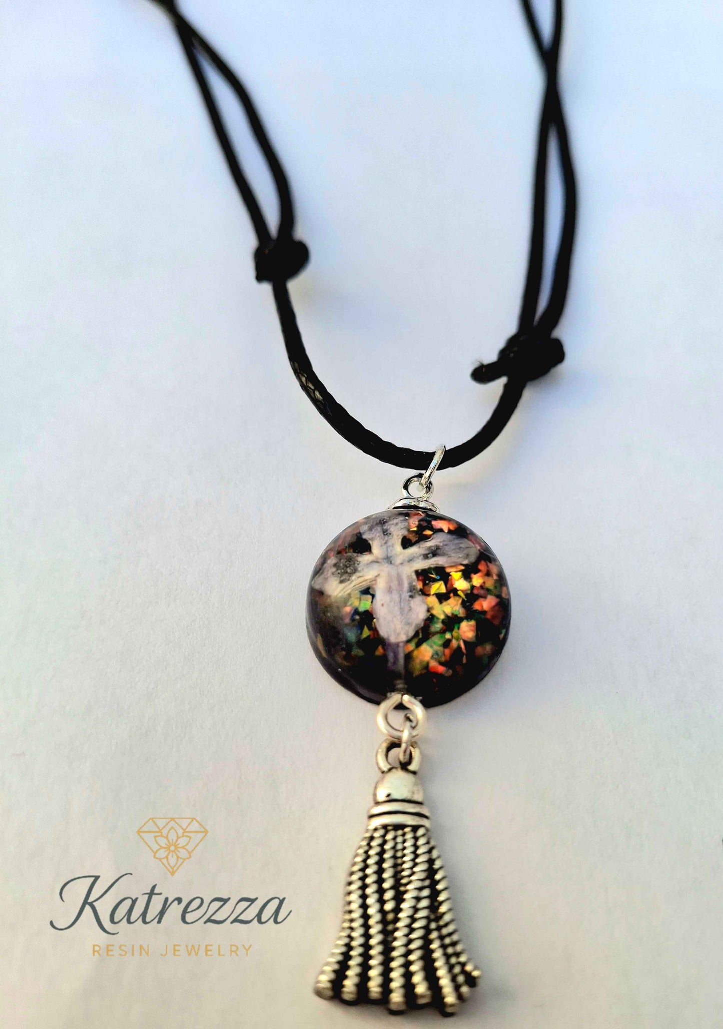 “Round resin pendant with preserved lilac flower and glitter accents, finished with silver tassel charm – Katrezza handmade jewelry.”