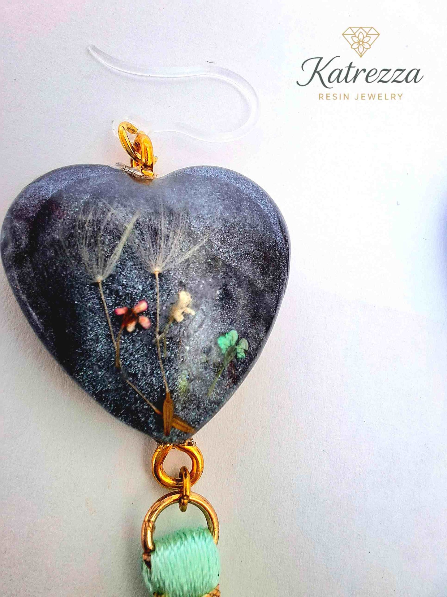 “Close-up of handmade resin earrings with dandelions and tiny flowers preserved inside.”