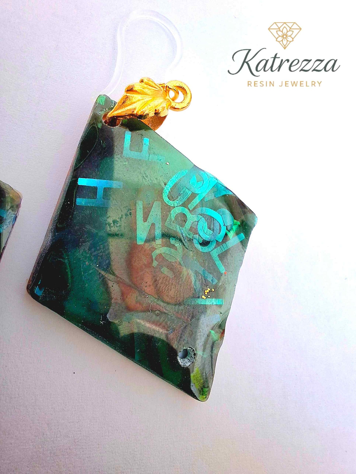 “Green resin earrings with shimmering blue letters and embedded details, geometric double-sided design.”