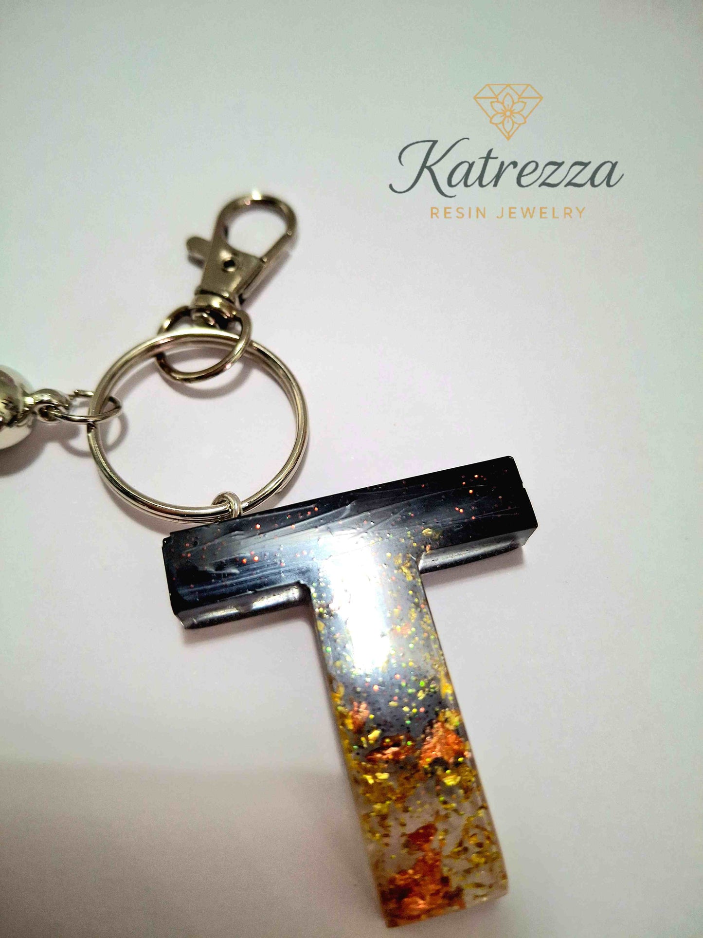 Resin letter T keychain with black resin and shimmering gold foil, handmade by Katrezza