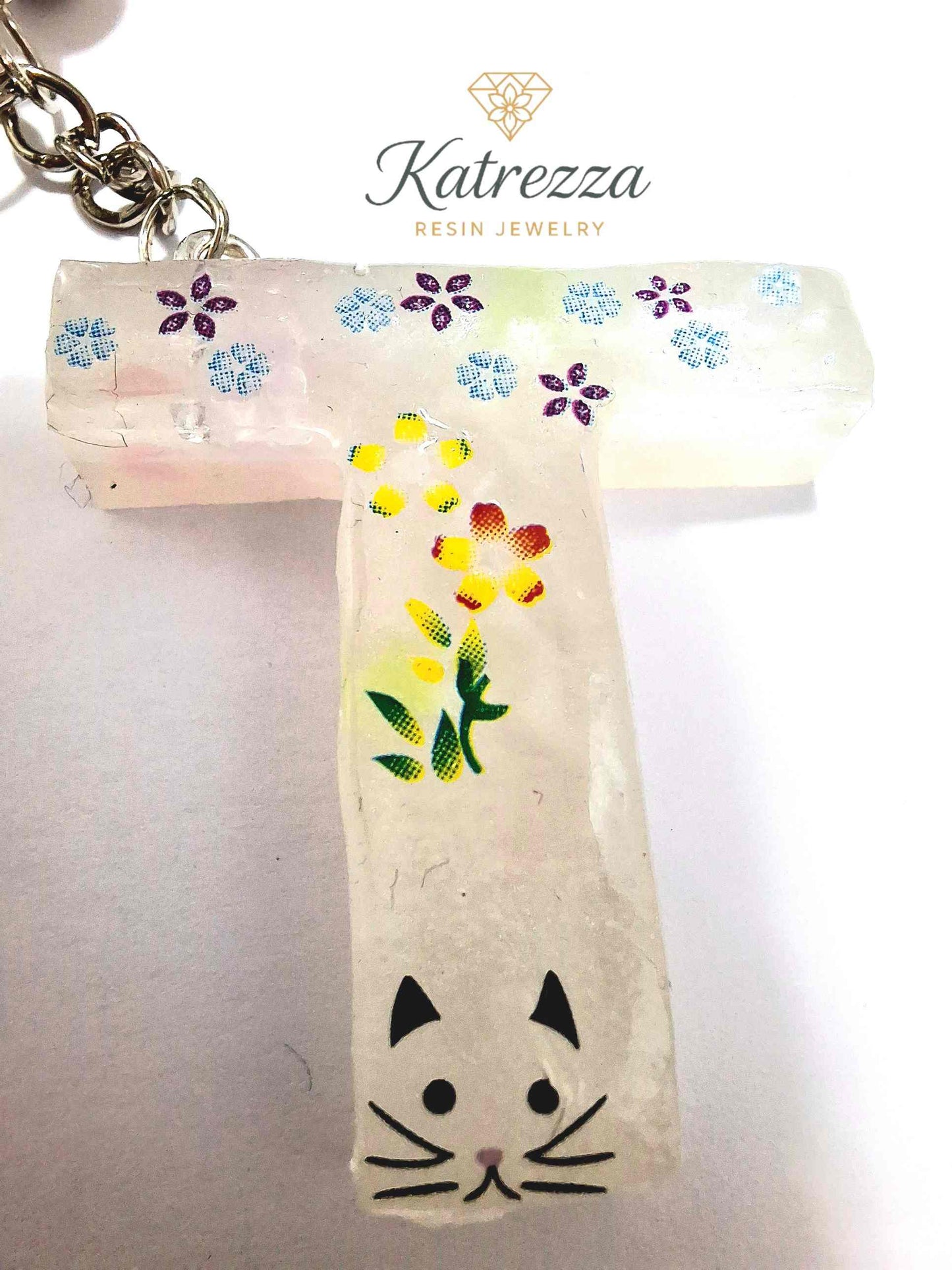 Glow-in-the-dark resin T keychain with colorful flowers and cat face.