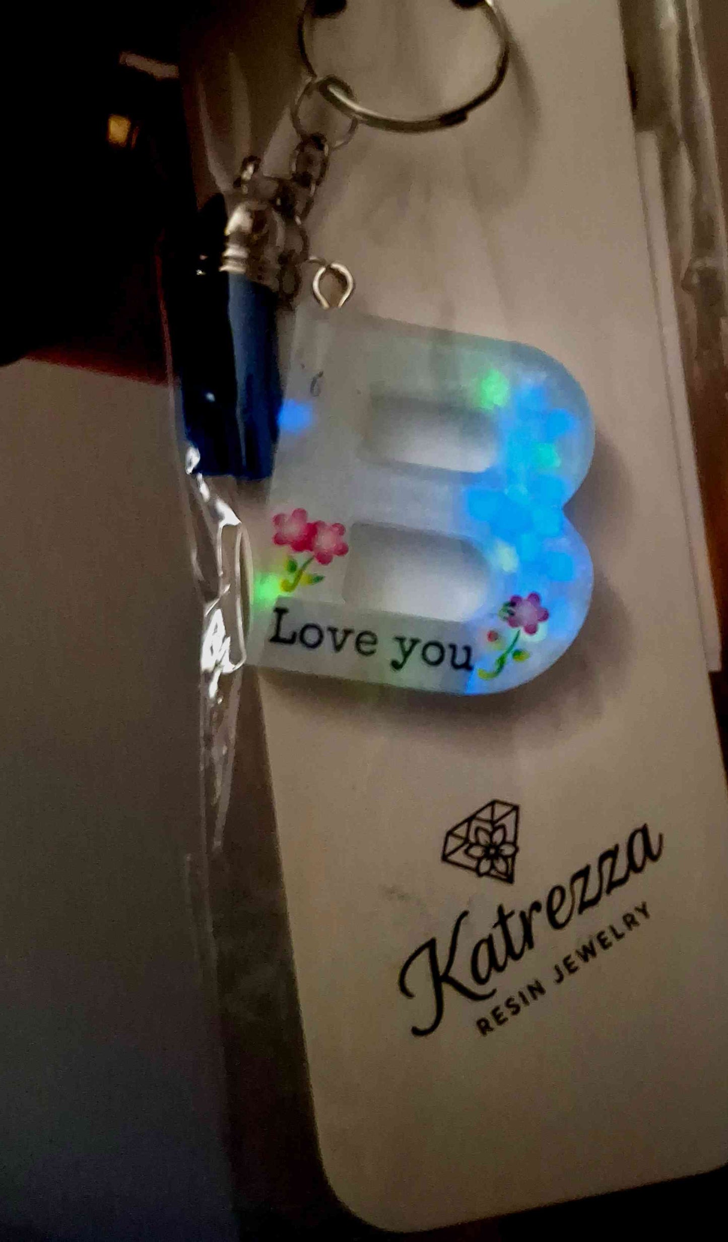 “Close-up of handmade resin letter B keychain with flowers and Love You text, glowing effect.”