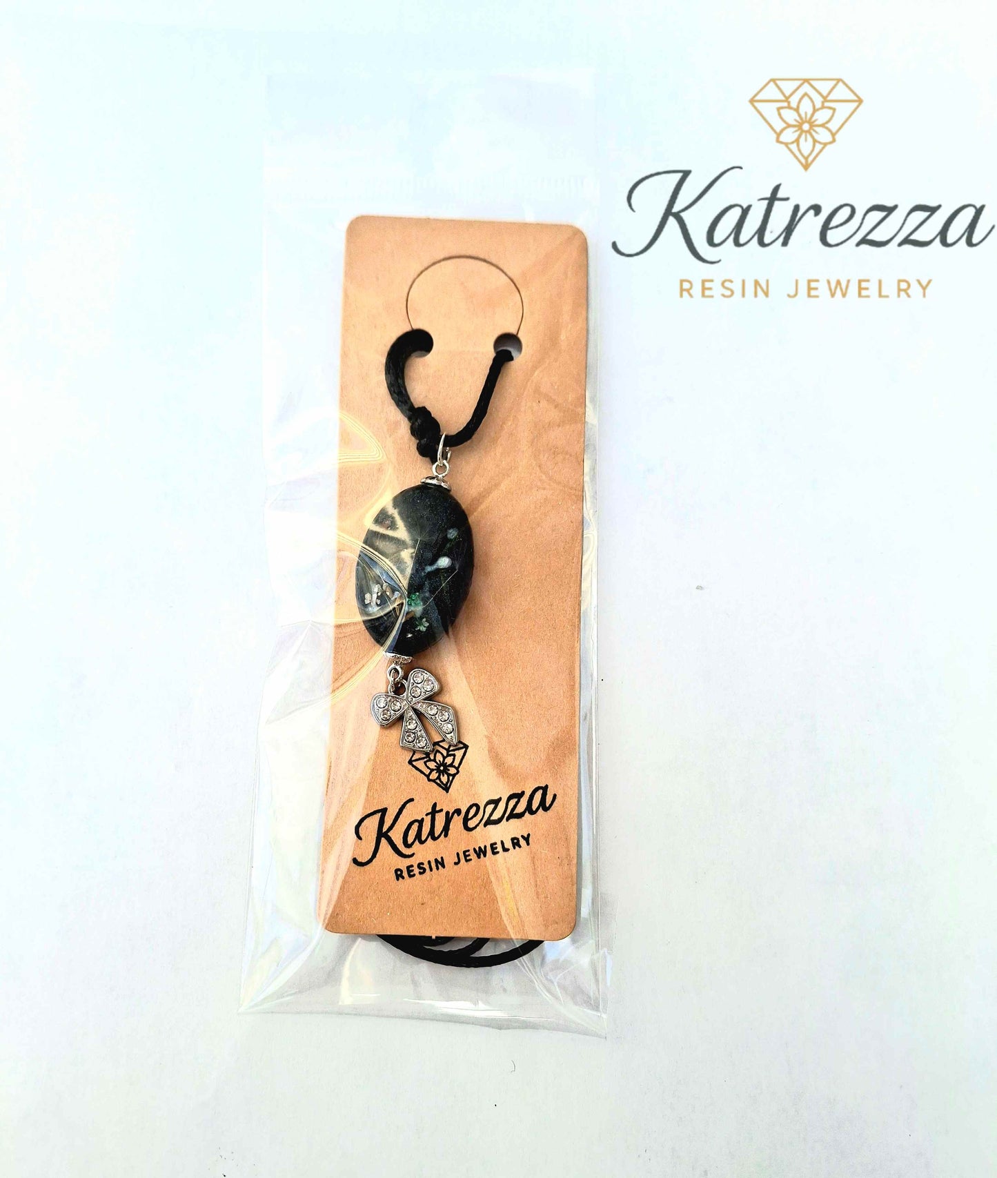 “Black oval resin pendant necklace with preserved Queen Anne’s Lace flowers, dandelion seeds, and silver bow charm on black cord – Katrezza resin jewelry packaging.”