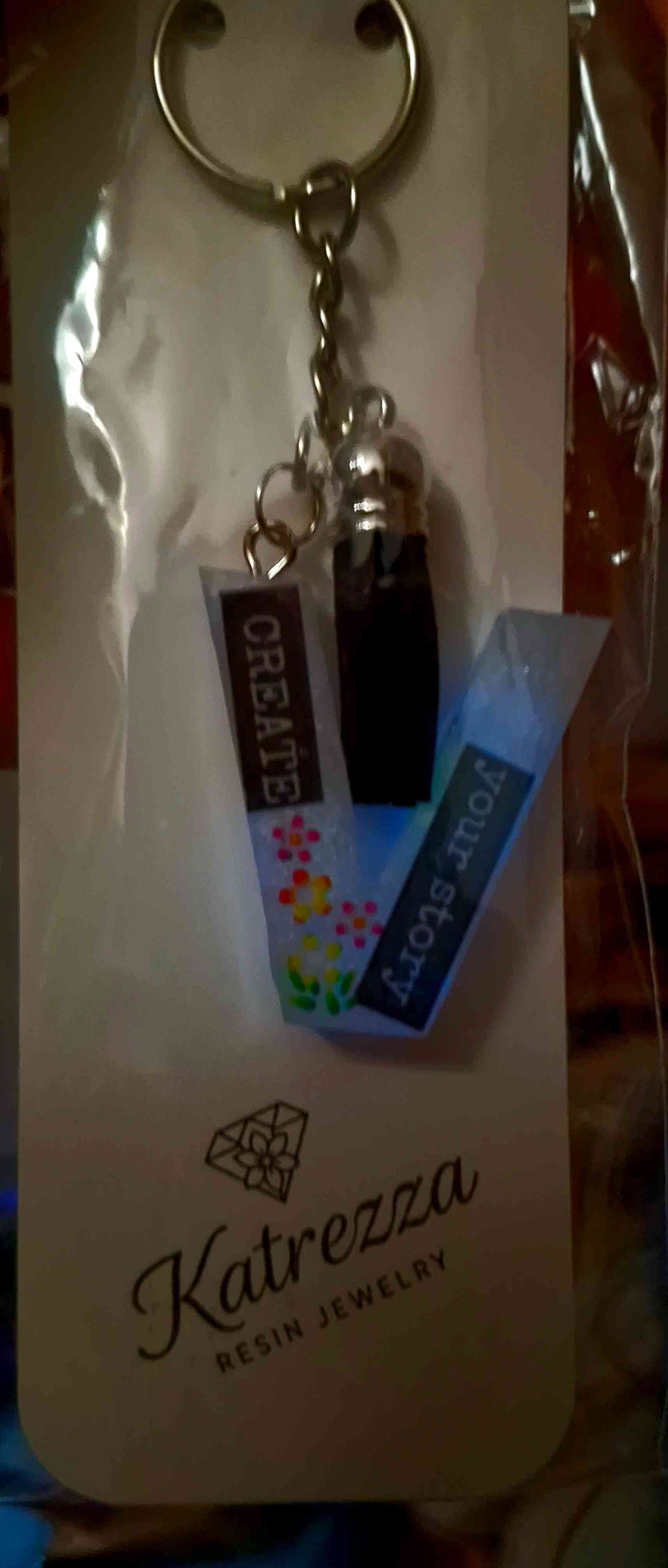 Resin letter V glow keychain in packaging with tassel charm attached.