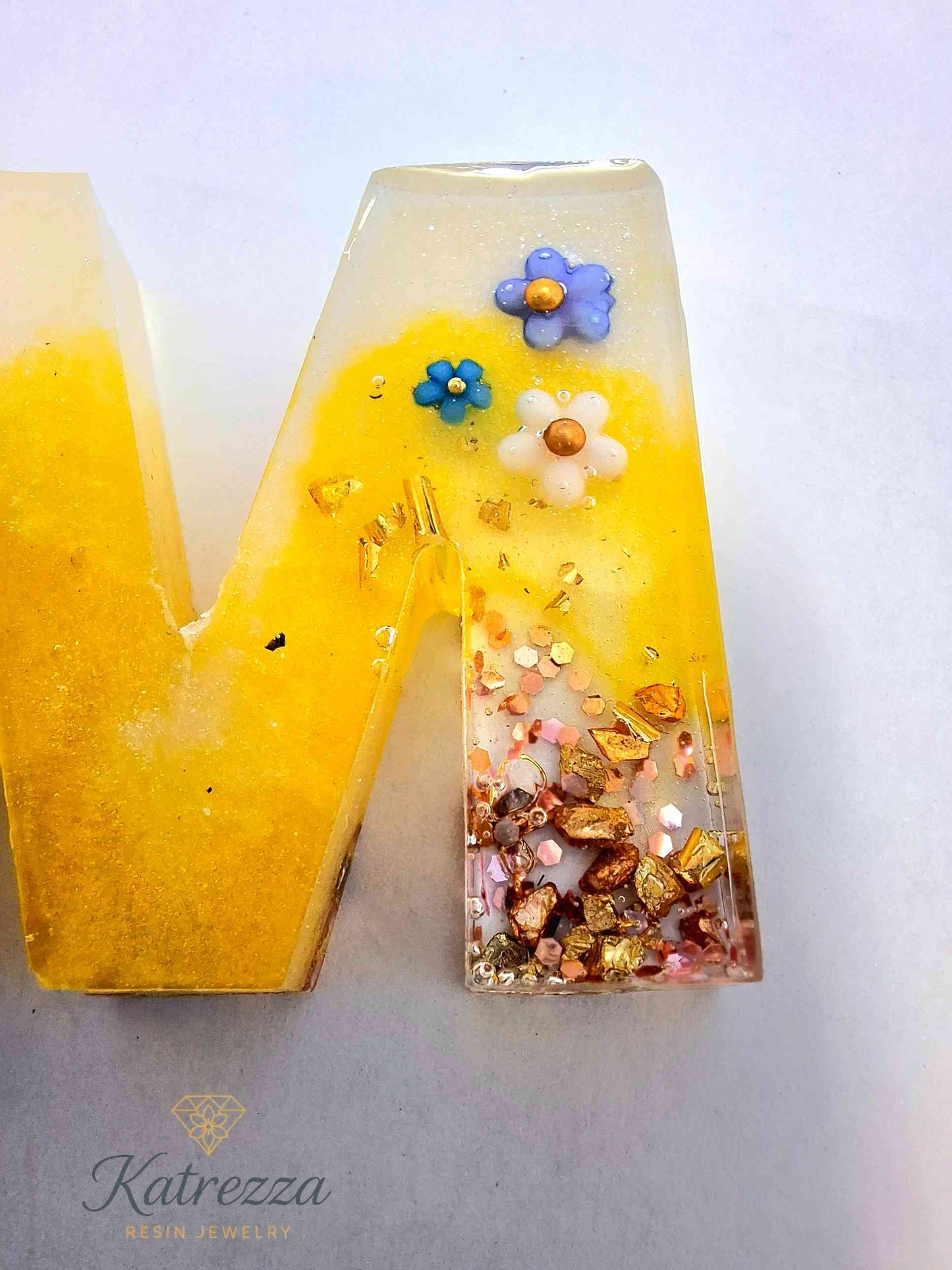 Resin letter M keychain close-up with embedded mini flowers.