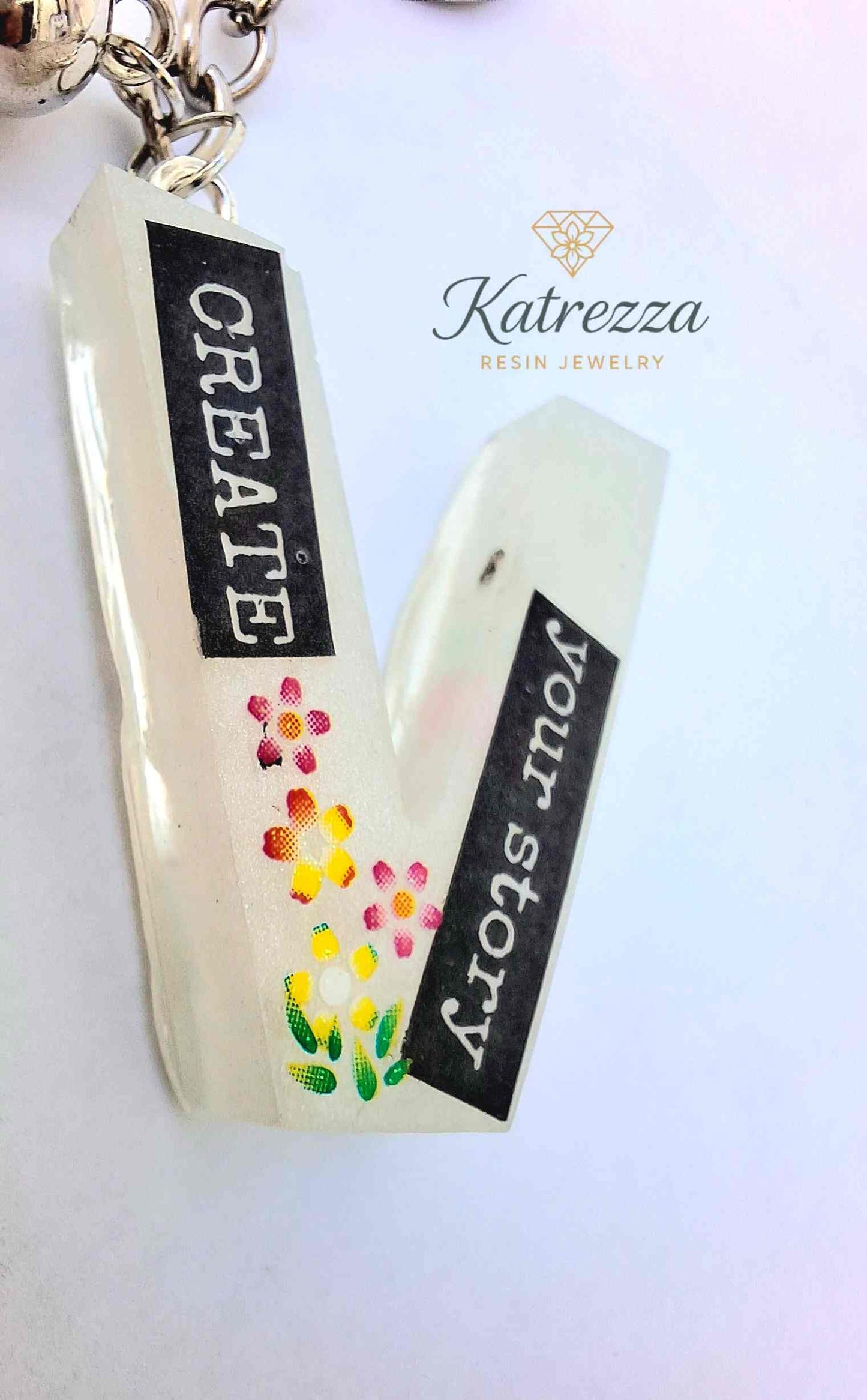Angled view of resin V keychain with glow effect and floral design.