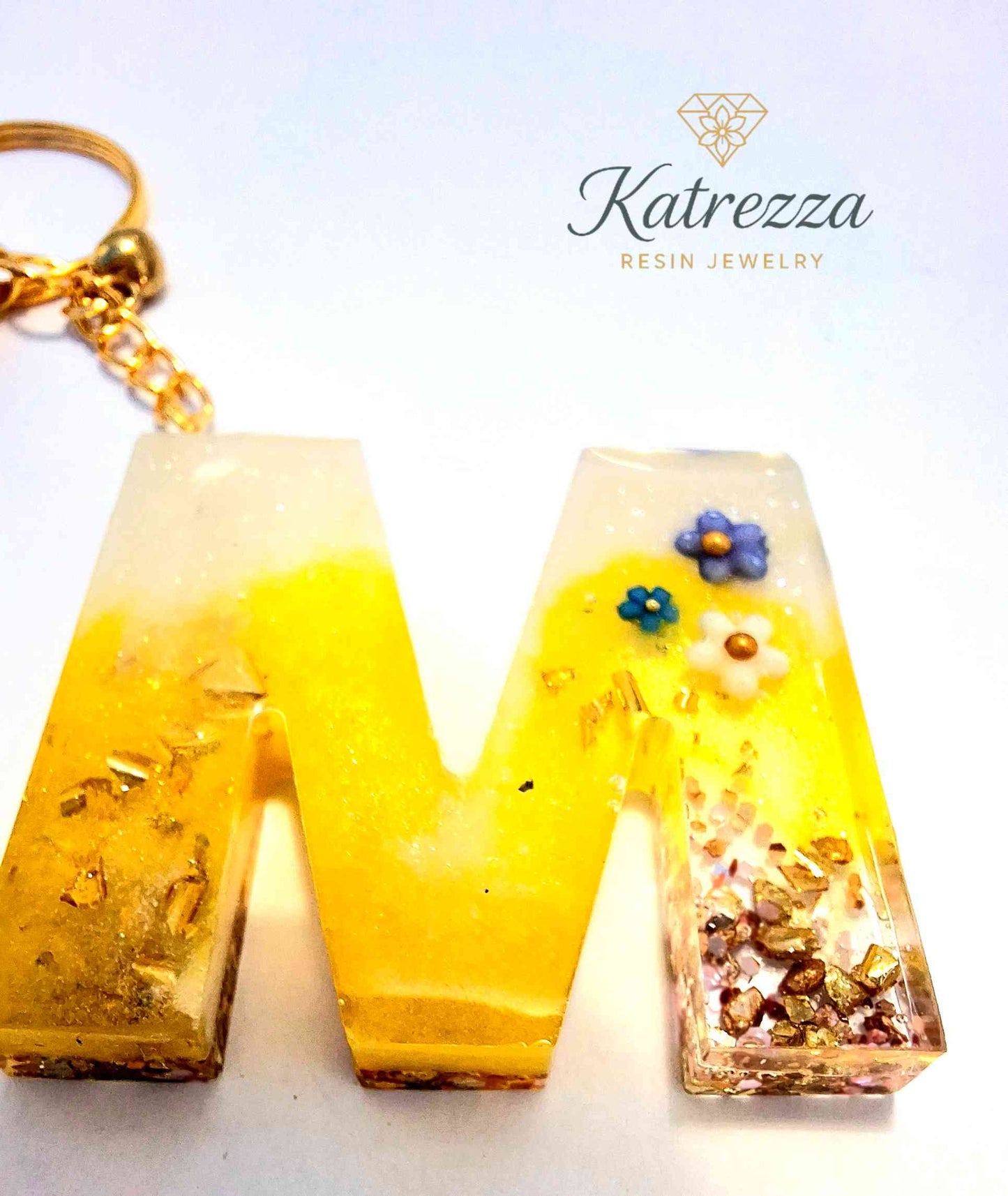 Bright yellow resin M keychain with flowers and gold accents.