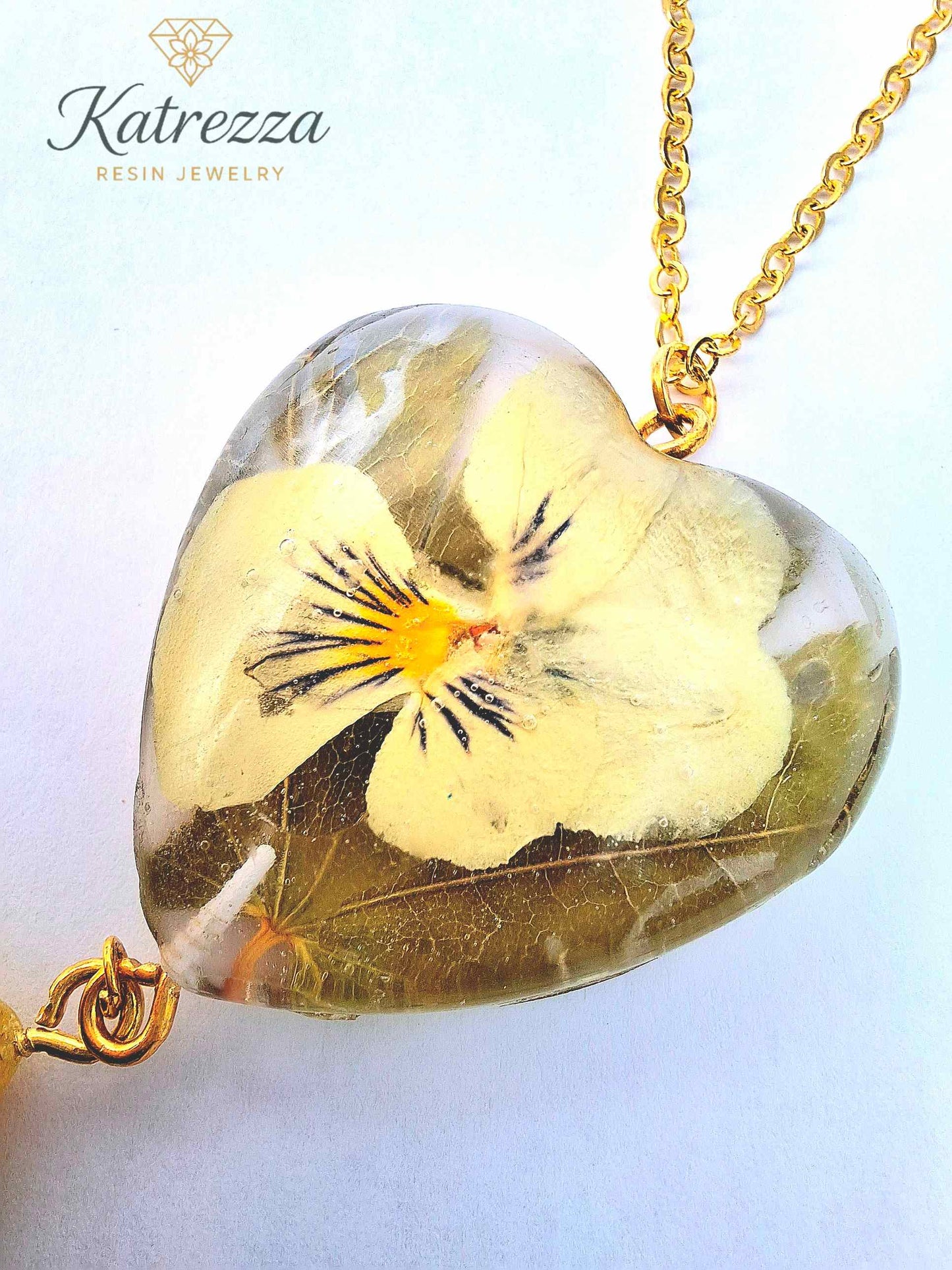 “Heart resin pendant with preserved real pansy flower inside, gold chain detail – Katrezza handmade jewelry.”