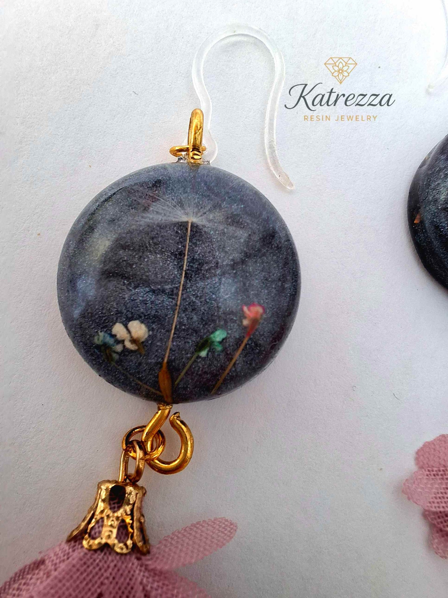 “Black resin earring with real flowers and dandelion seed, pink tassel charm, gold accent, and silicone hypoallergenic hook – 6.5 cm length.”
