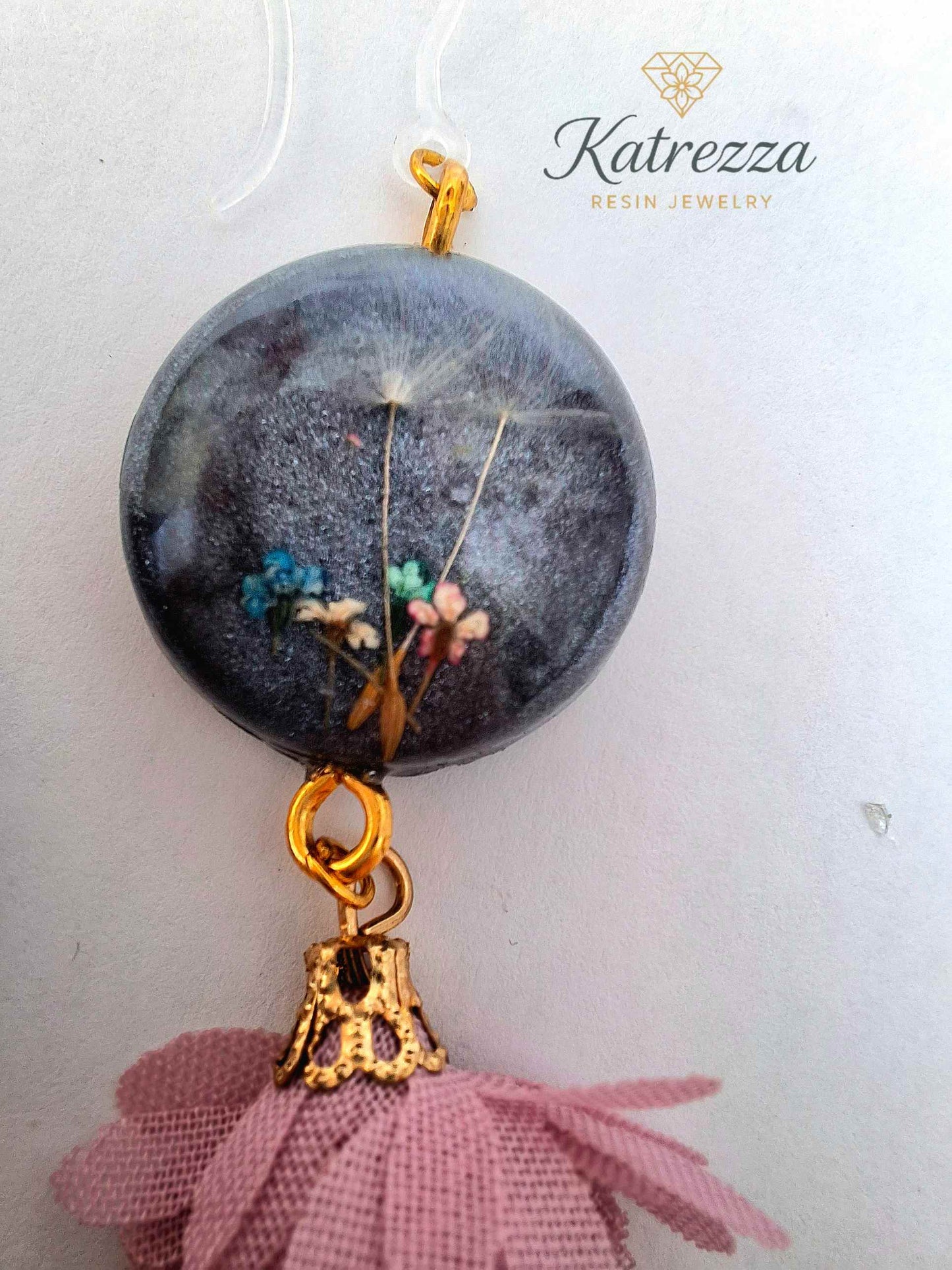 “Black resin earring with real flowers and dandelion seed, pink tassel charm, gold accent, and silicone hypoallergenic hook – 6.5 cm length.”