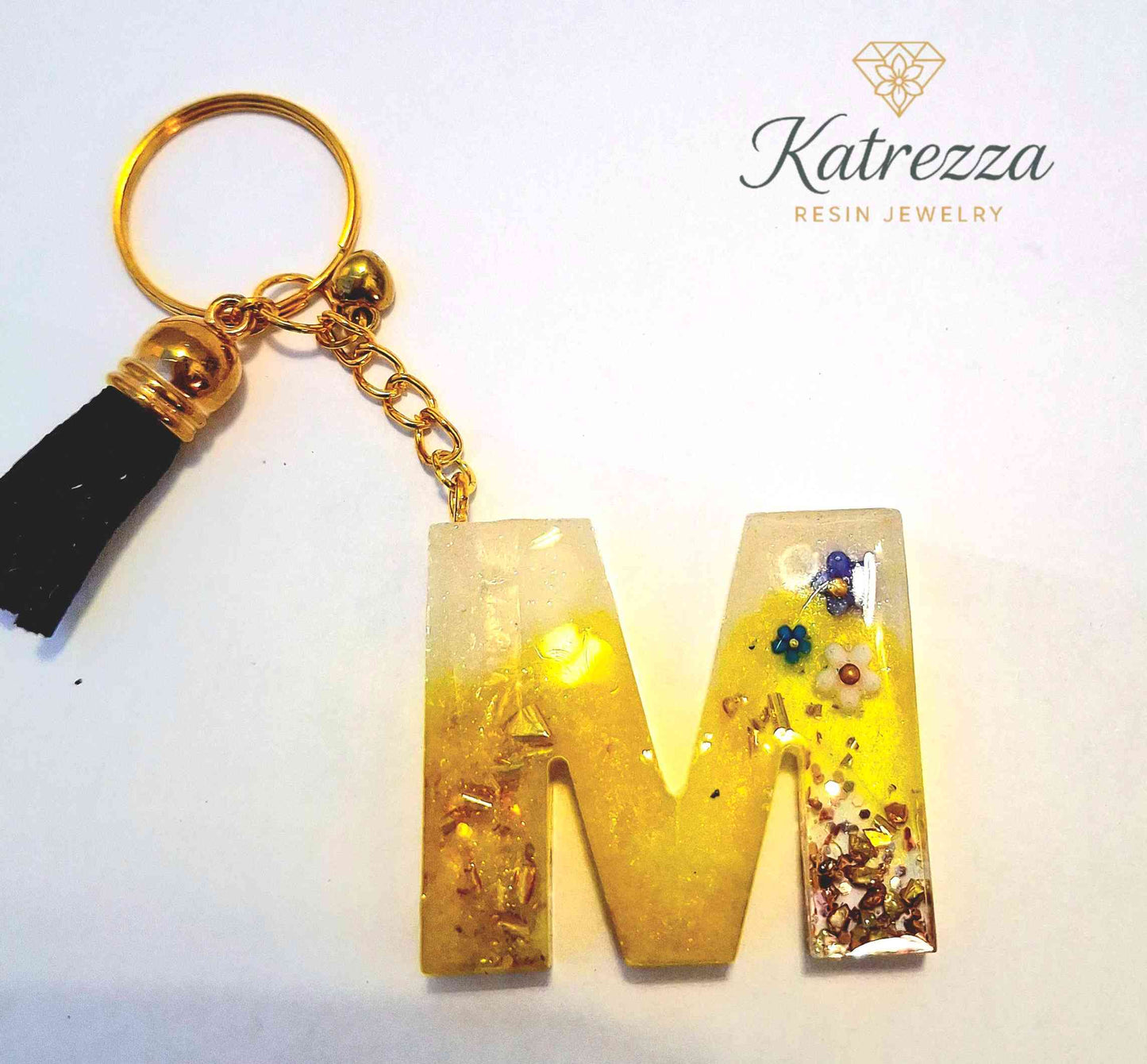 Detailed resin M keychain with flowers and glitter flakes.