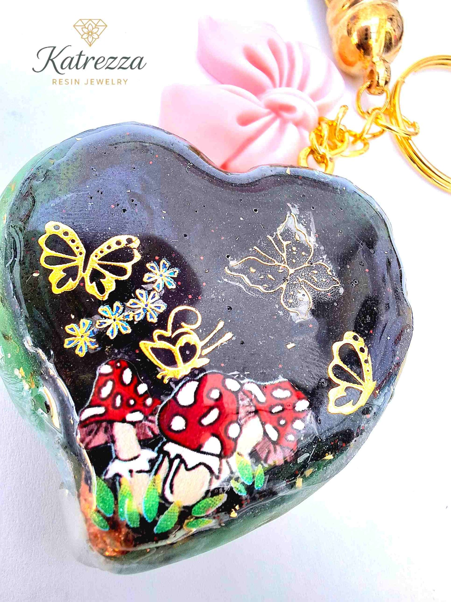 "Close-up of resin heart charm with golden butterflies and mushroom design – Katrezza Jewelry Imperfection Collection"