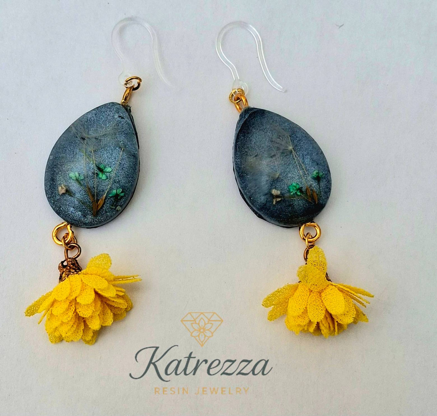 “Teardrop resin earrings with preserved flowers and dandelion seeds, dark resin background, yellow tassels, and silicone hypoallergenic ear hooks – 7 cm.”