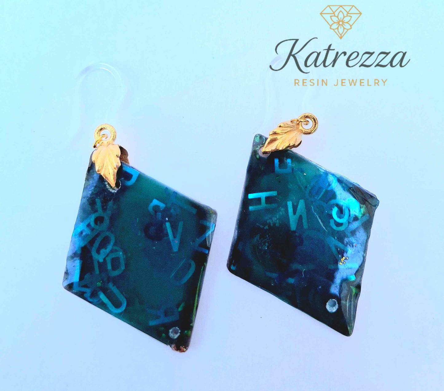 “Green resin earrings with shimmering blue letters and embedded details, geometric double-sided design.”