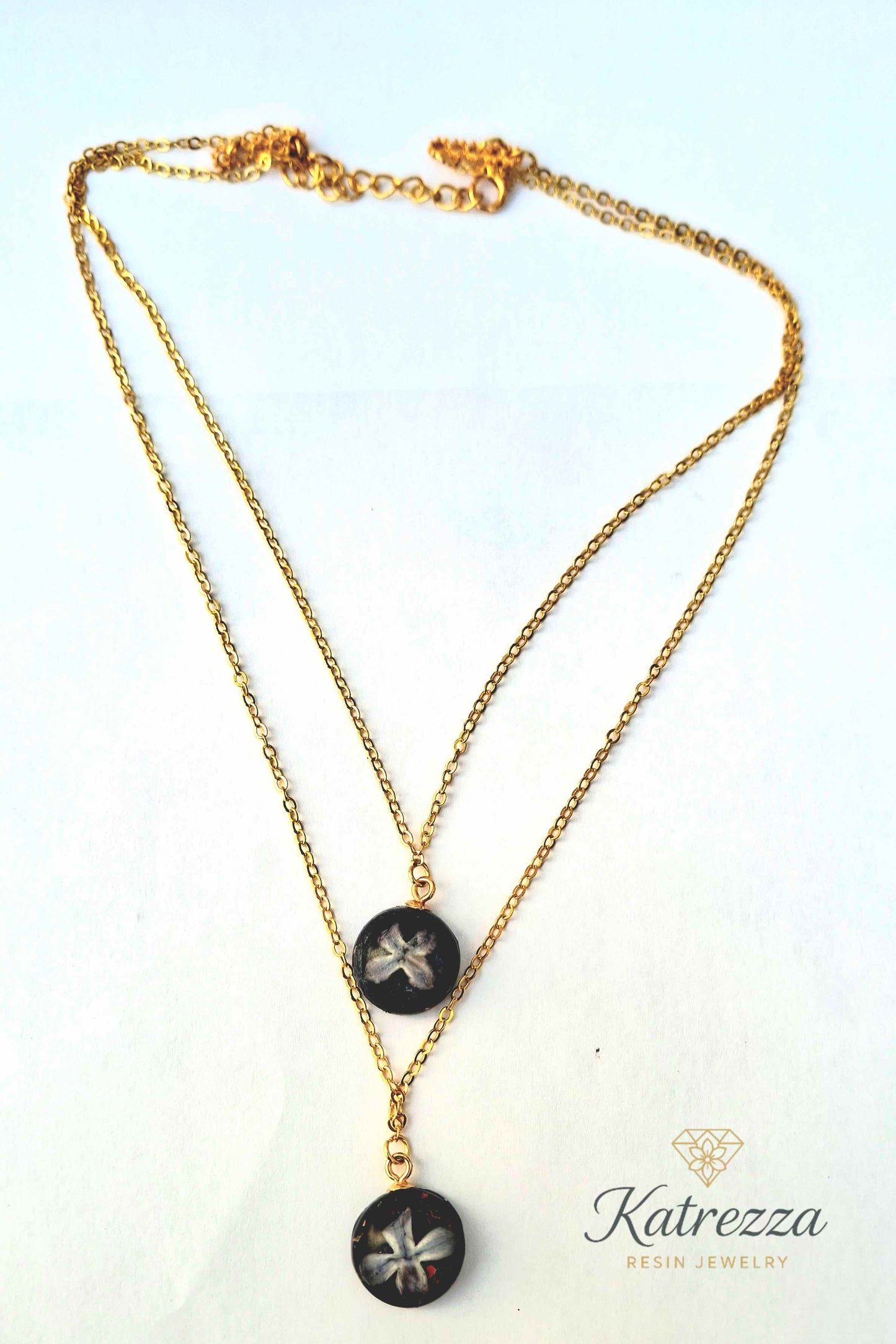 Full view of handmade double chain necklace with two resin pendants, real lilac flowers, glitter accents, and adjustable gold chain.