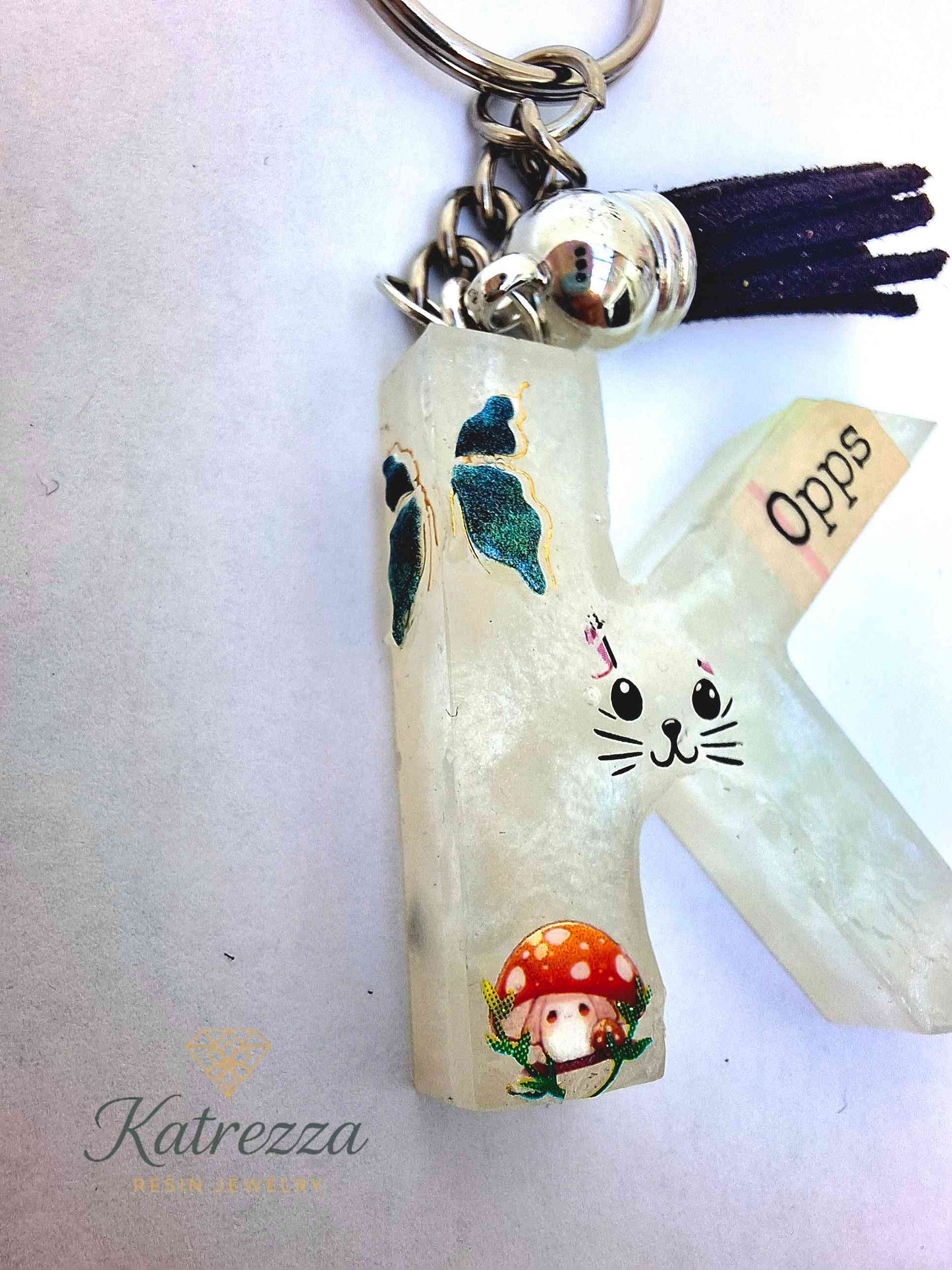 Handmade resin K keychain with stickers, tassel, and shiny finish.