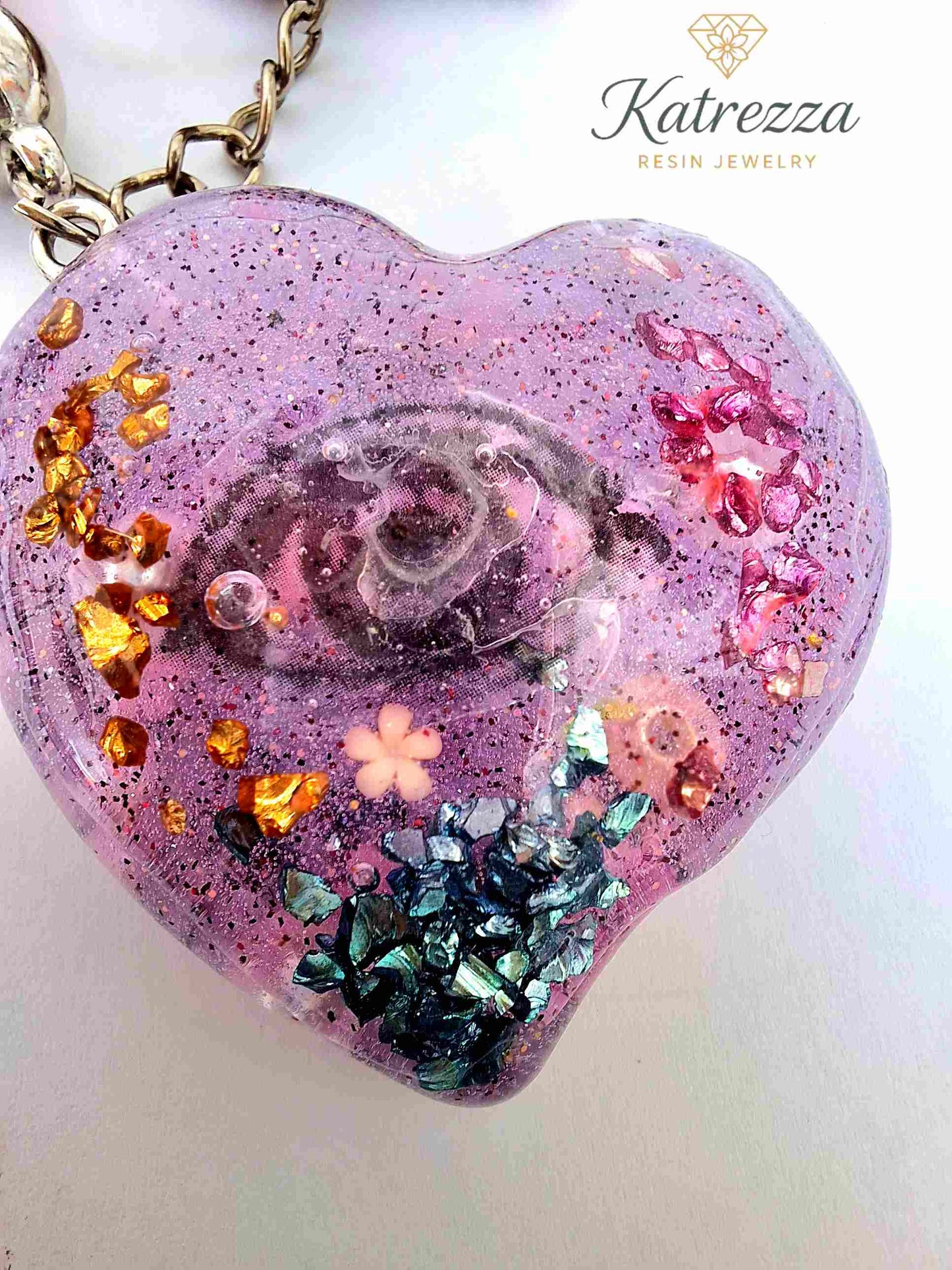 Close-up of resin heart keychain with gold, blue, and pink flakes inside.