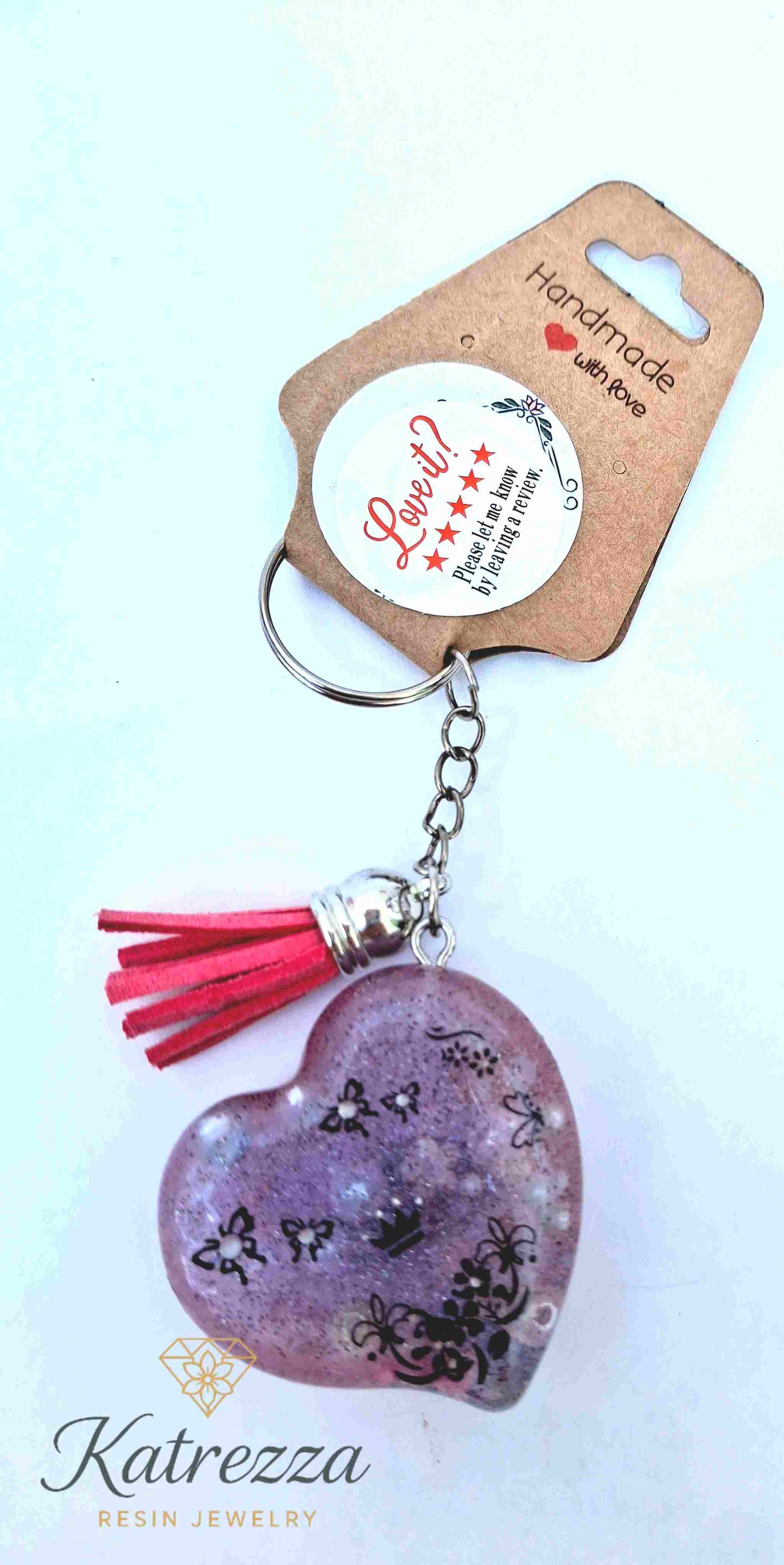 Handmade purple resin heart keychain with black floral patterns and red tassel.