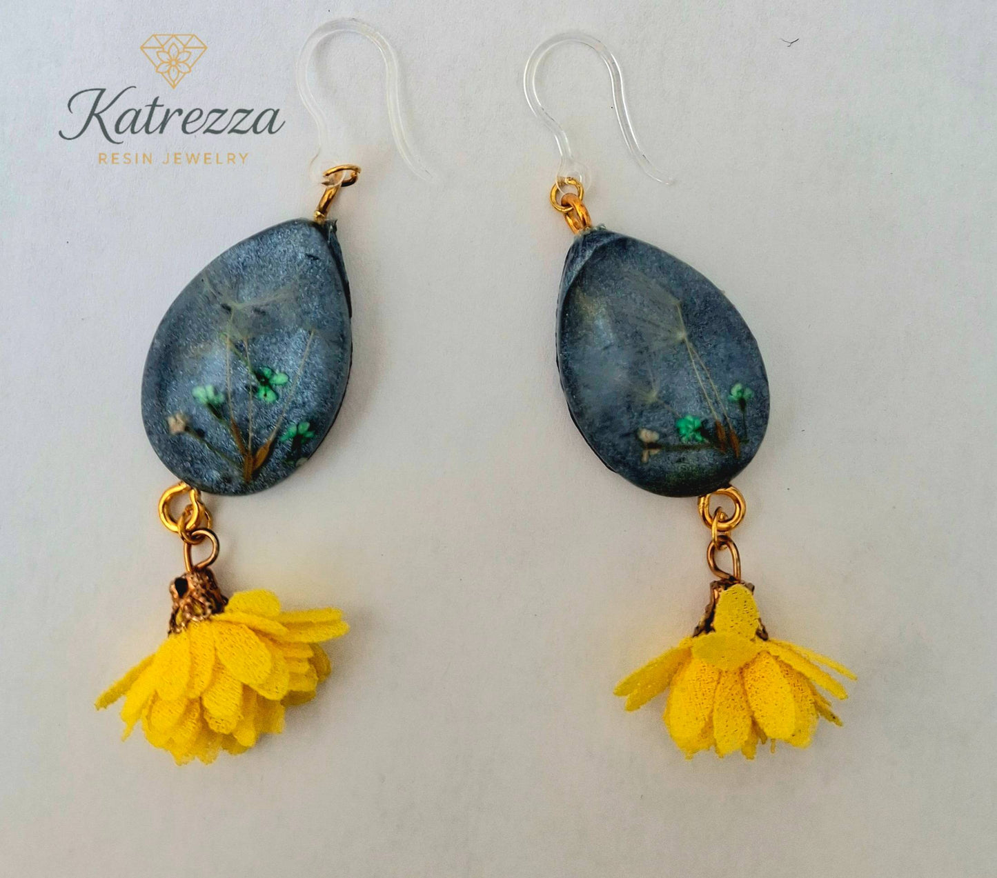 “Teardrop resin earrings with preserved flowers and dandelion seeds, dark resin background, yellow tassels, and silicone hypoallergenic ear hooks – 7 cm.”