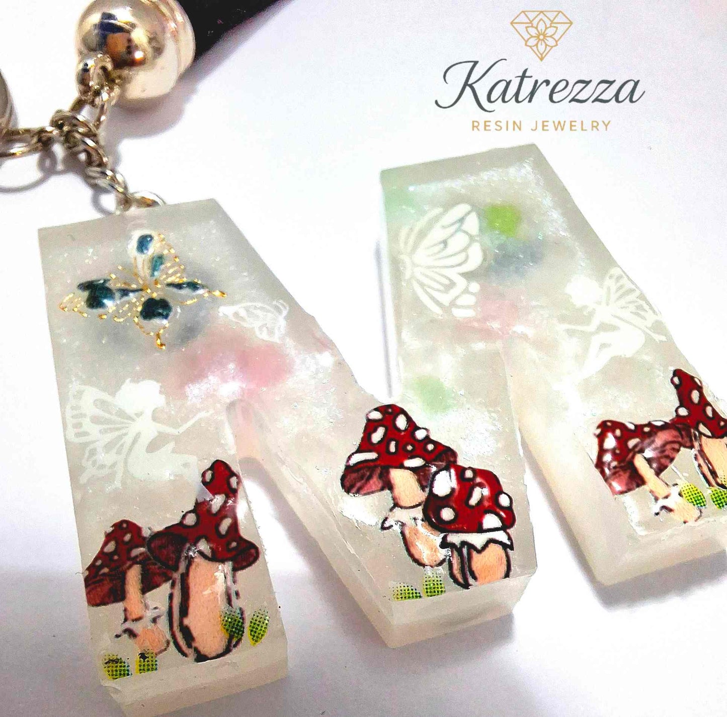 Close-up of resin letter M keychain showing fairy silhouette and mushrooms.