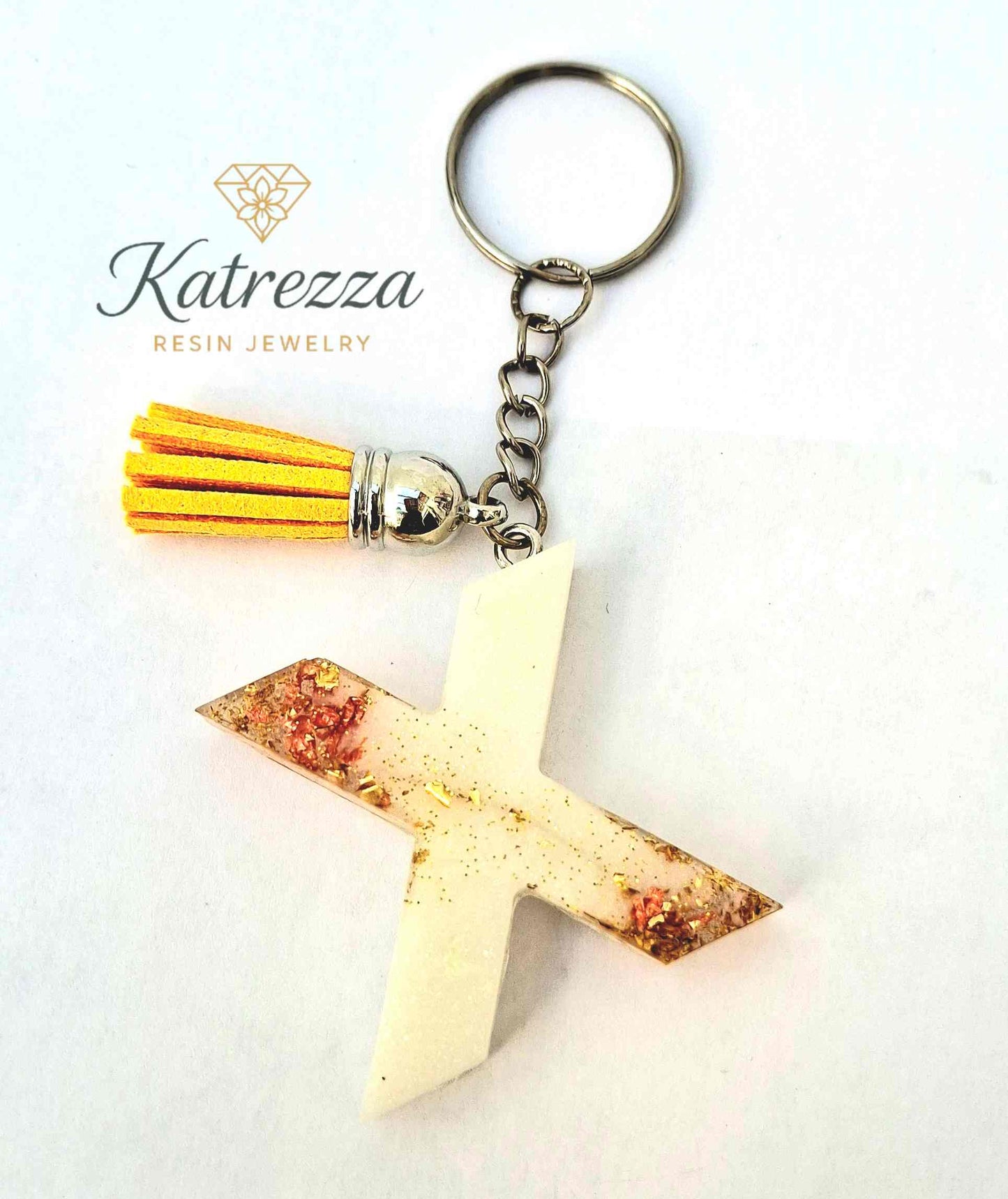 Handmade resin X keychain with yellow tassel and shimmering accents.