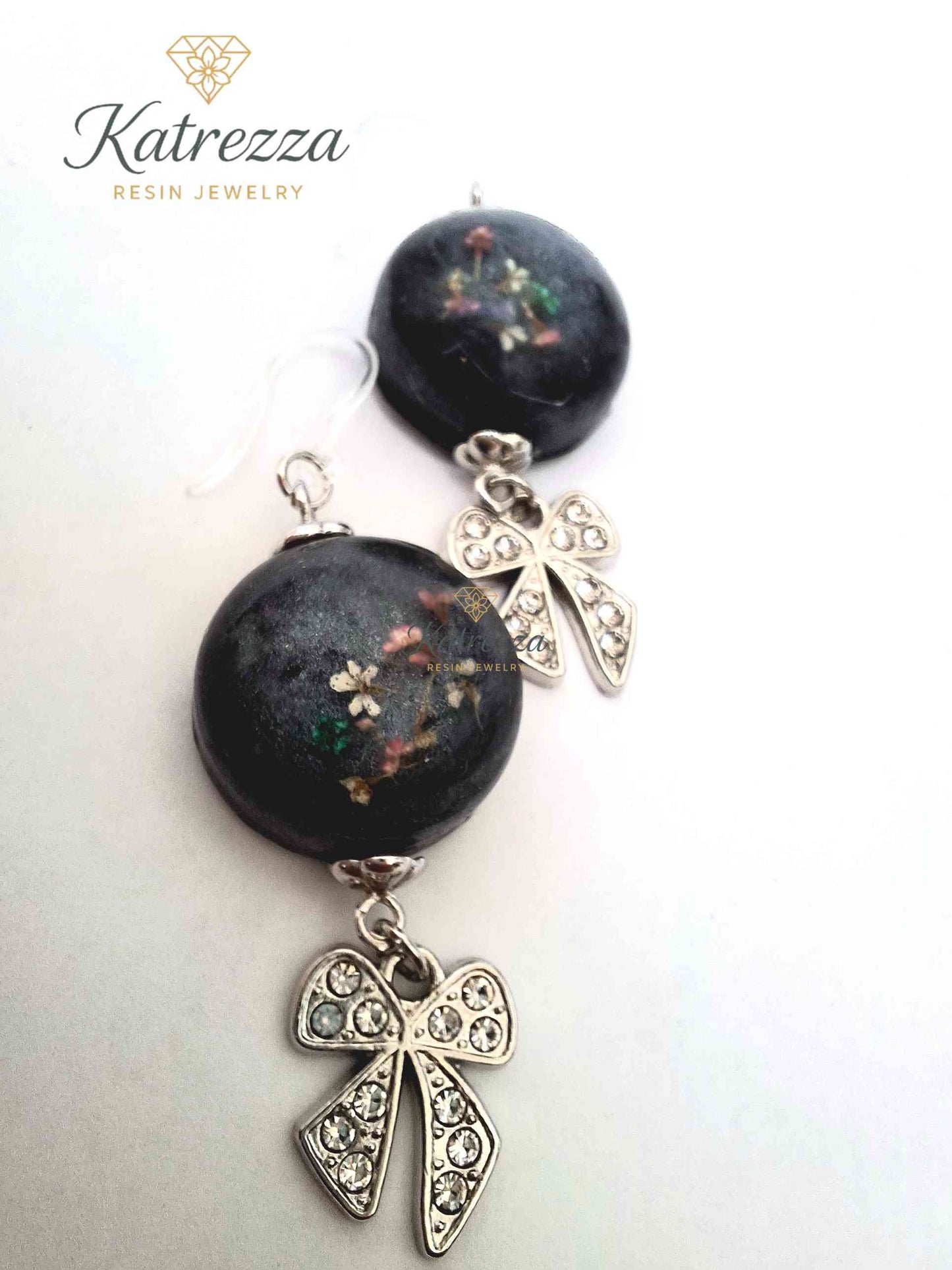 Close-up of round black resin earrings with preserved flowers and crystal bow dangle