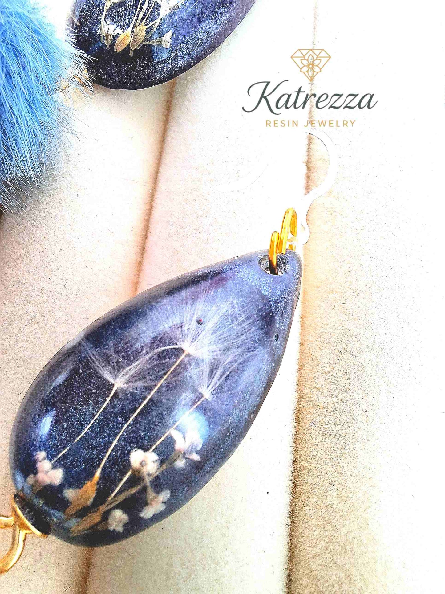 "Close-up of teardrop resin earring with glittery grey-black resin, tiny real flowers, dandelion seeds, and blue pom-pom charm – Katrezza Jewelry"