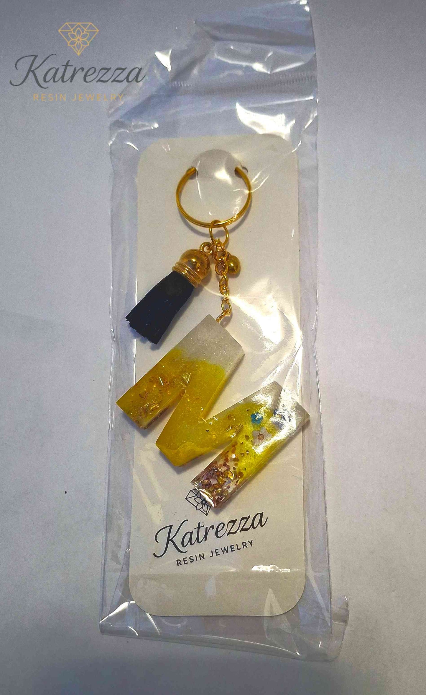 Packaged resin M keychain with gold foil shimmer.