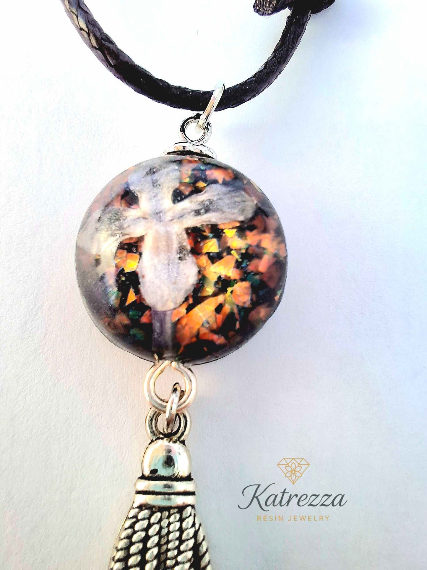 “Round resin pendant with preserved lilac flower and glitter accents, finished with silver tassel charm – Katrezza handmade jewelry.”