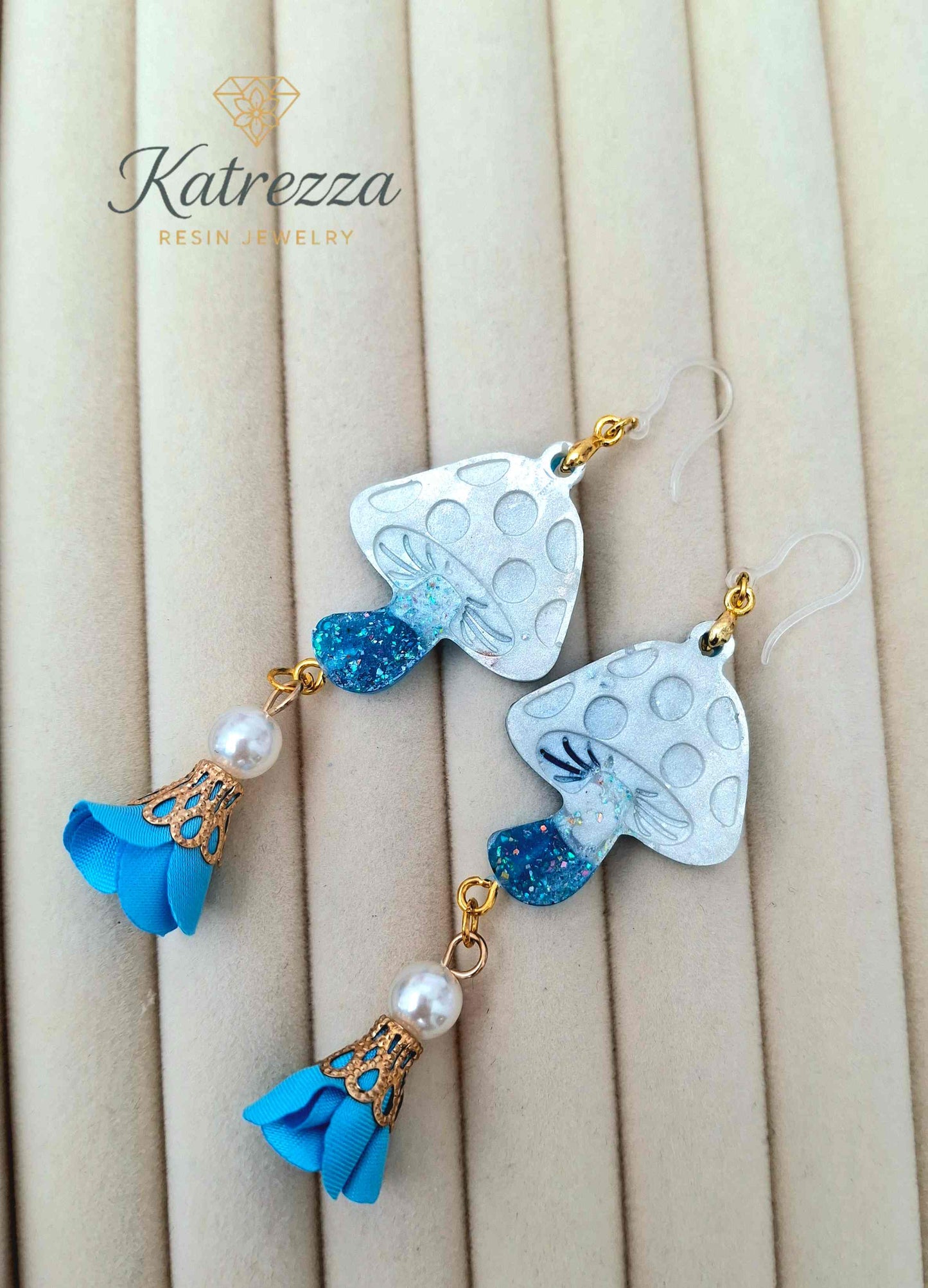 "Close-up of double-sided resin mushroom earrings showing glittery blue stems and textured white caps – Katrezza Jewelry"