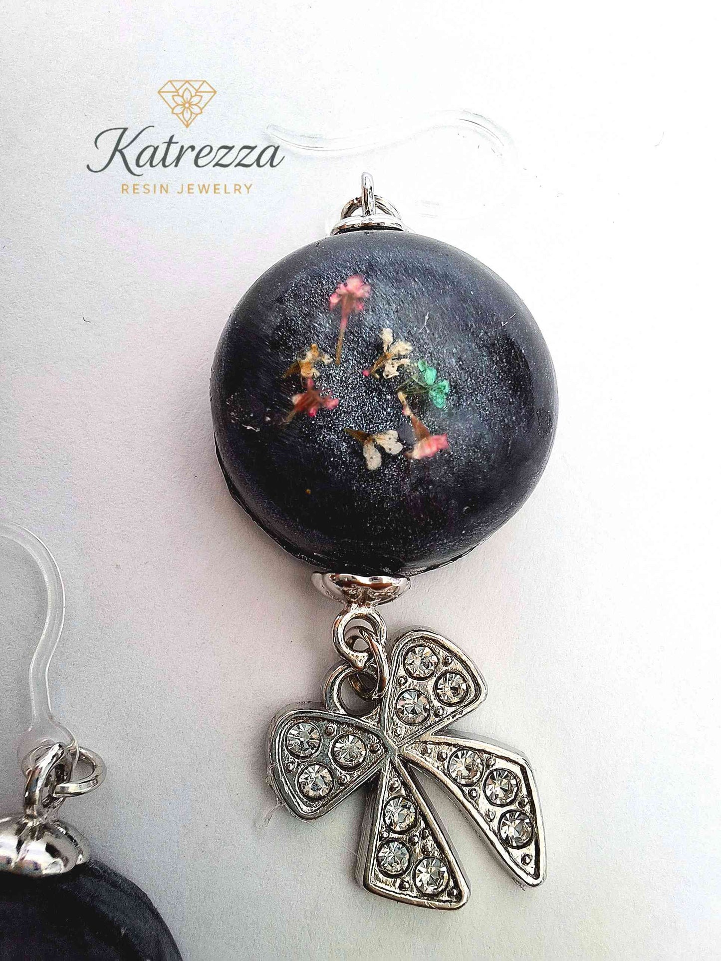 Close-up of round black resin earrings with preserved flowers and crystal bow dangle