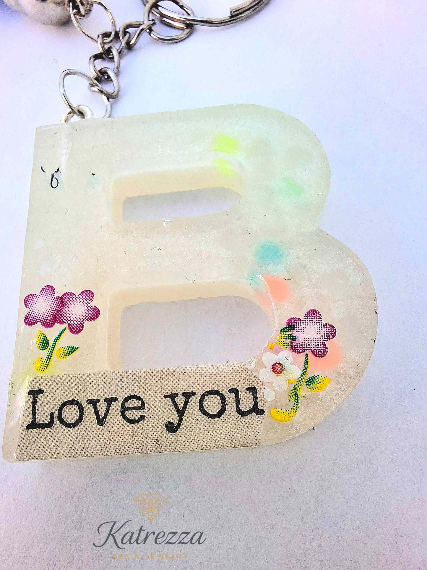 “Handmade resin letter B keychain with colorful flower accents and glowing finish.”
