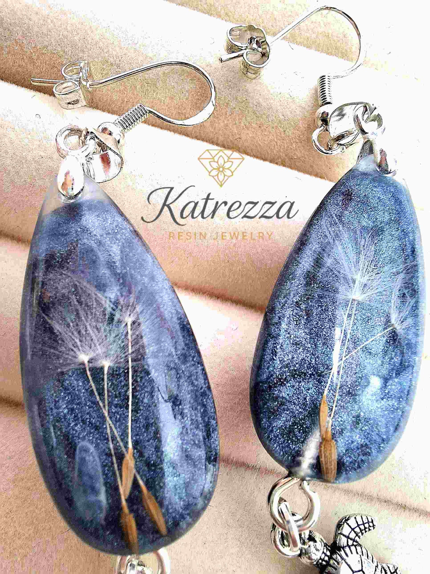 Handmade resin dandelion earrings displayed on jewelry box background.