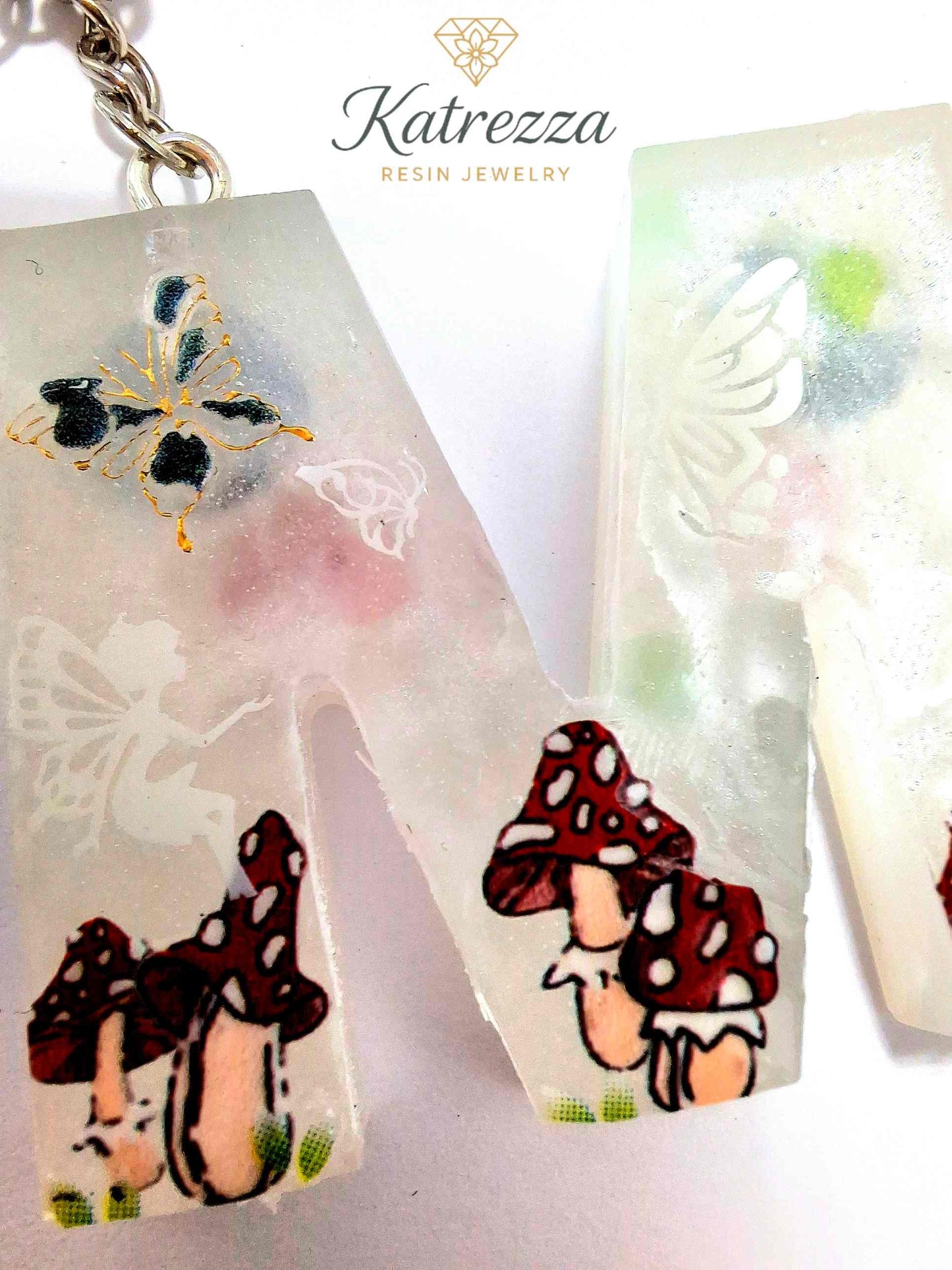 Artistic resin M keychain with mushrooms, butterflies, and fantasy details.