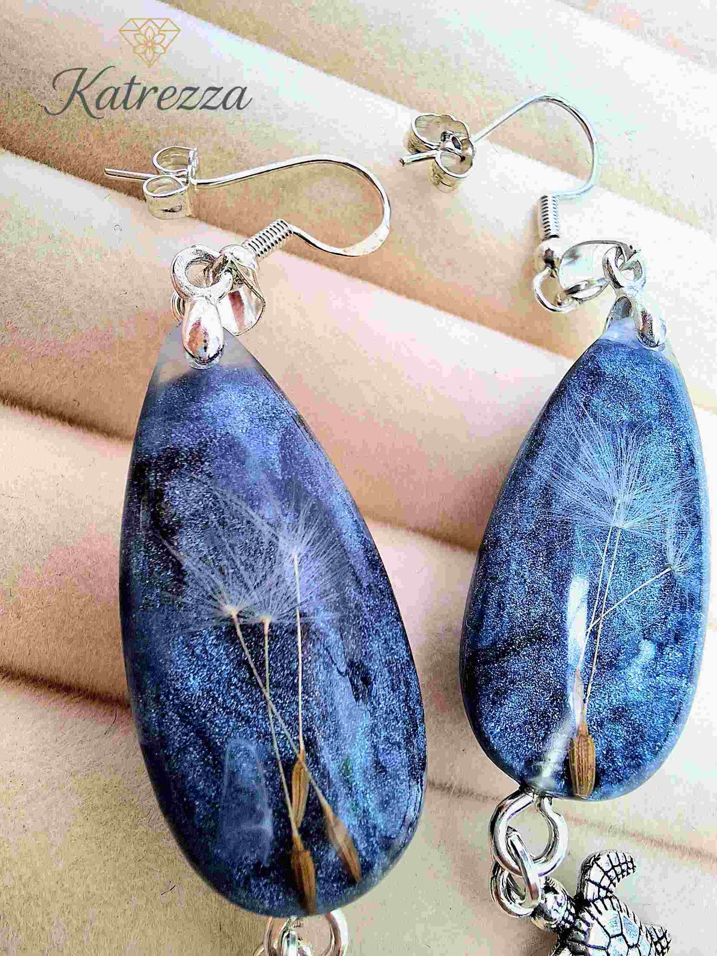 Close-up of handmade resin drop earrings with dandelion bouquet inside blue glitter resin