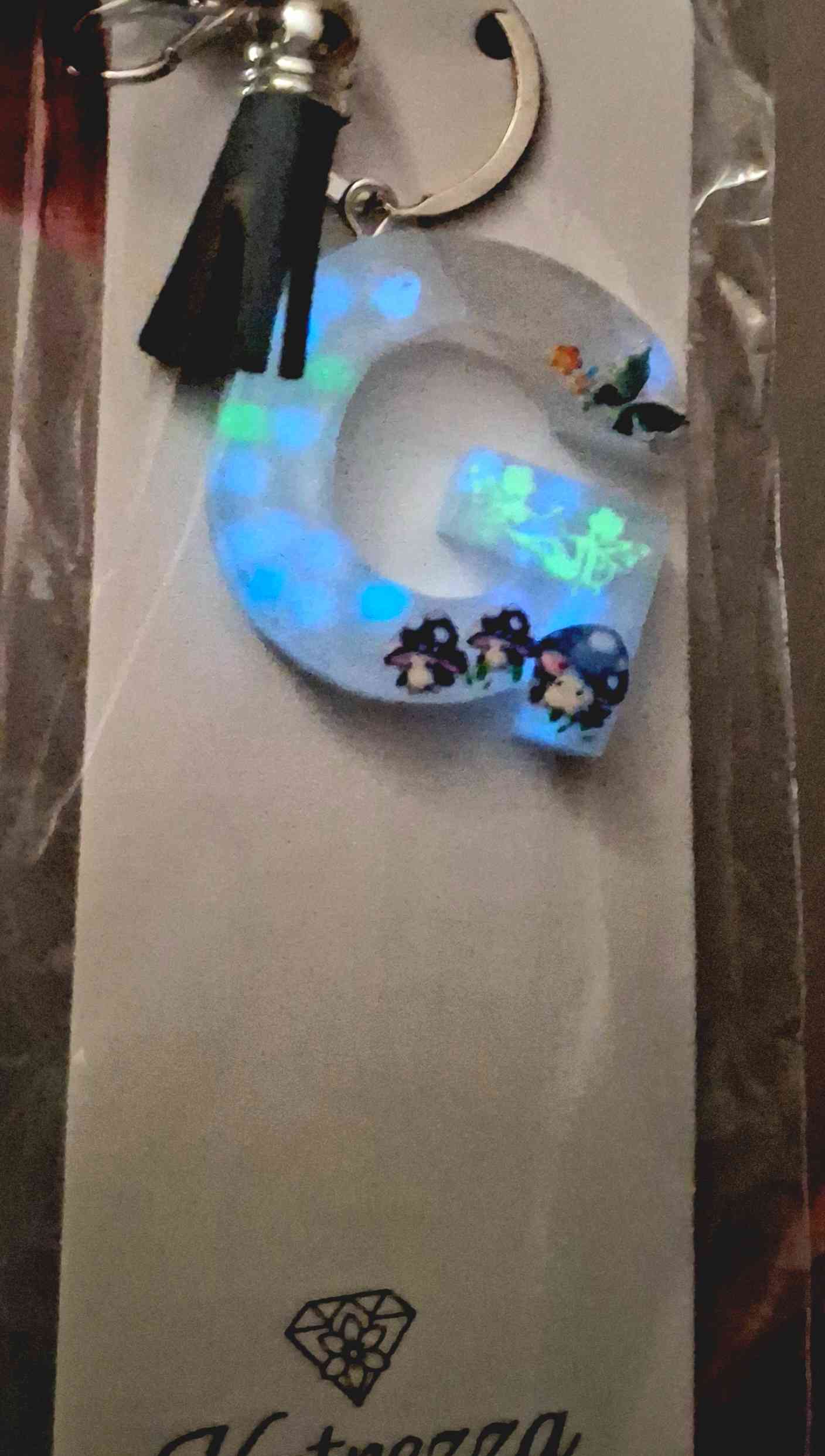 Glow-in-the-dark resin G keychain with mushroom stickers and butterfly detail.