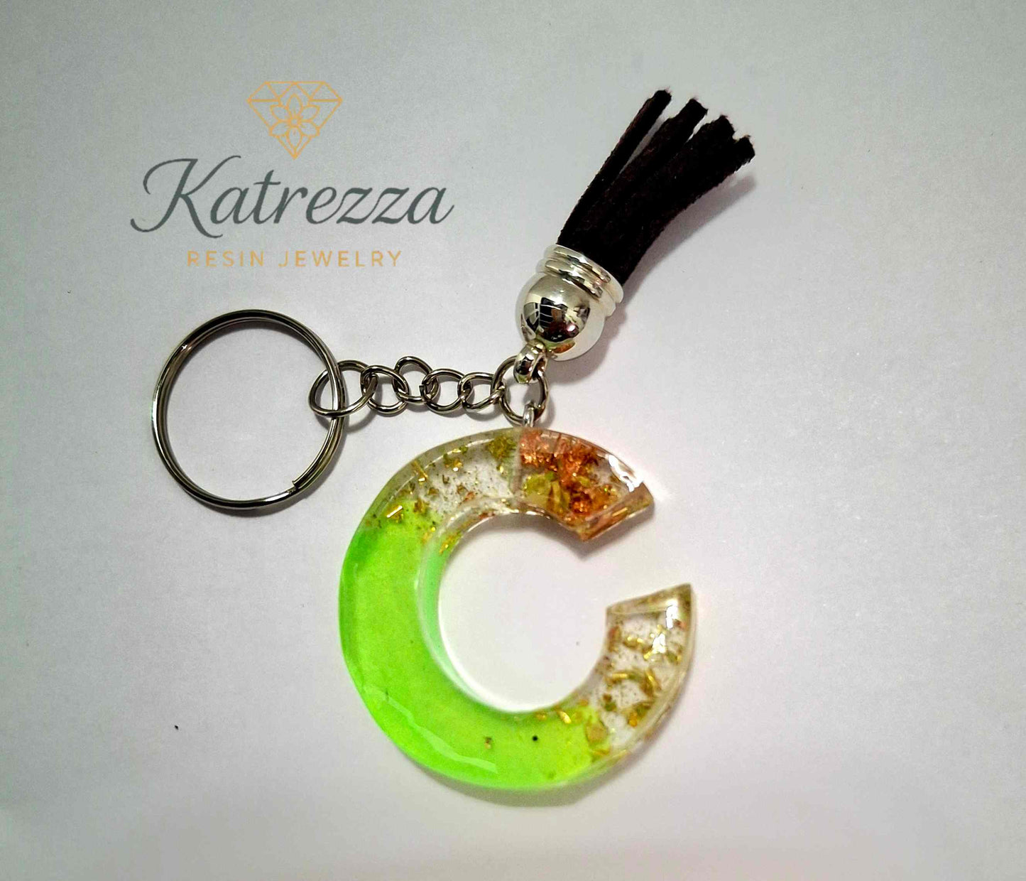 Green resin letter C keychain with black tassel and silver ring, decorated with gold and copper foil.