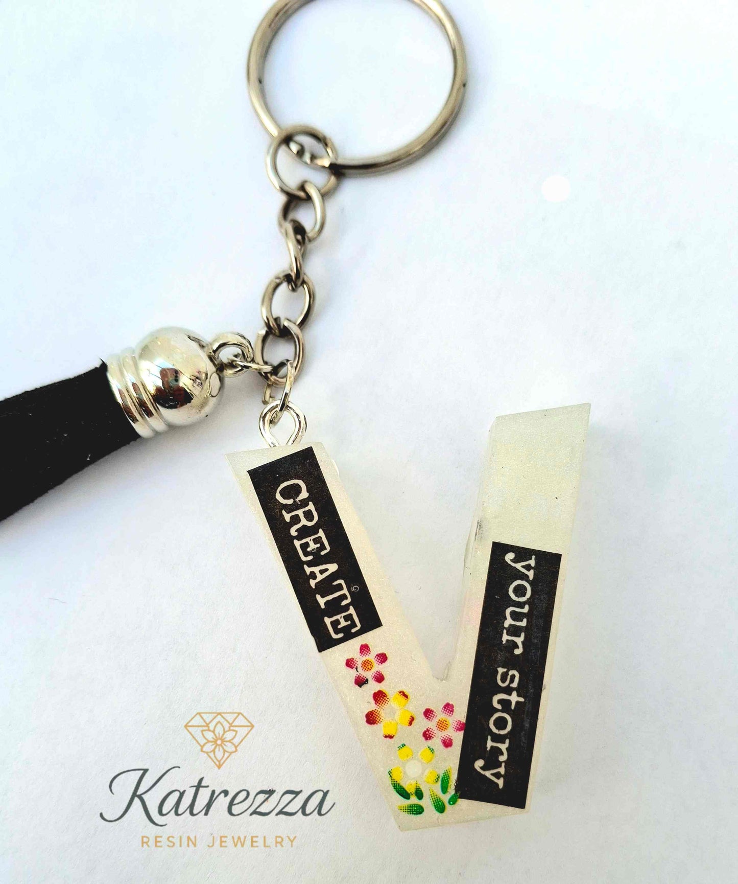 Close-up of glowing resin V keychain showing inspirational text and flowers.