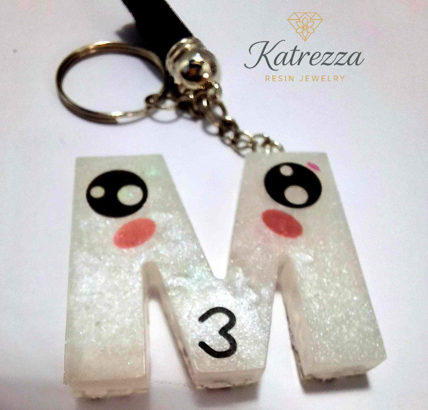 Resin letter M keychain with kawaii-style cute face design and tassel.