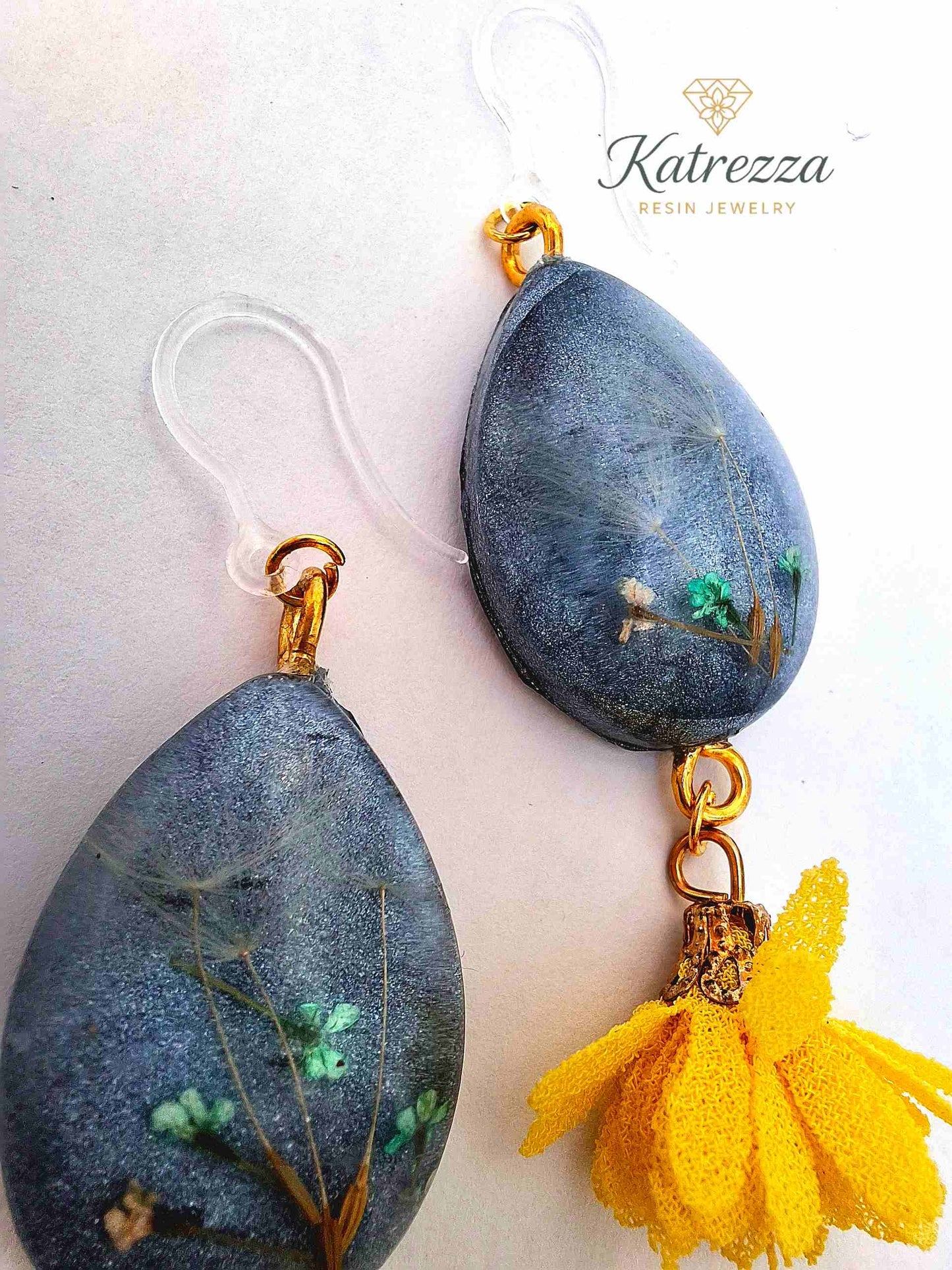“Handmade 7 cm teardrop resin earrings with real flowers and dandelion seeds, gold accents, yellow tassels, and hypoallergenic silicone hooks.”