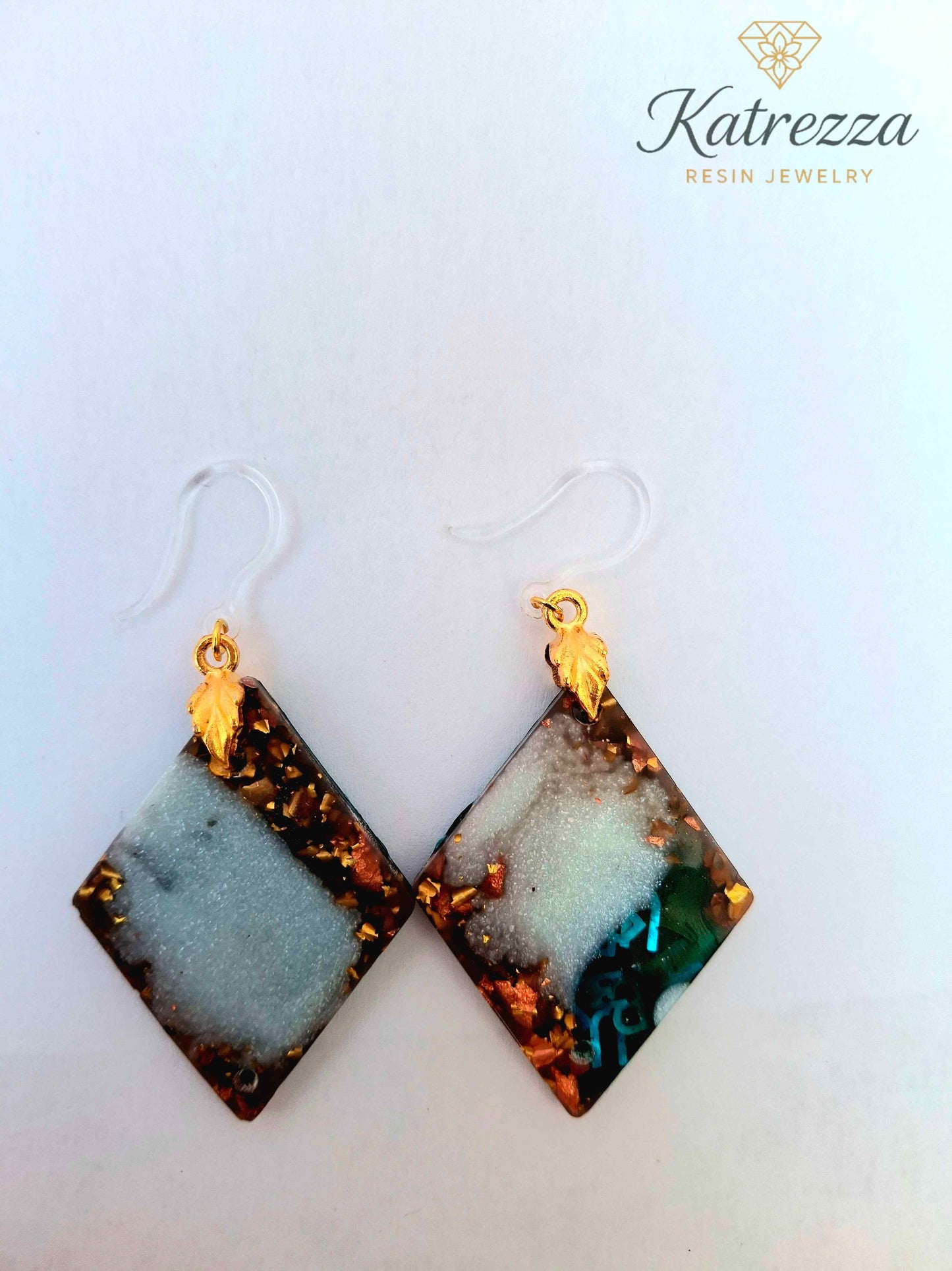 “Green resin earrings with shimmering blue letters and embedded details, geometric double-sided design.”