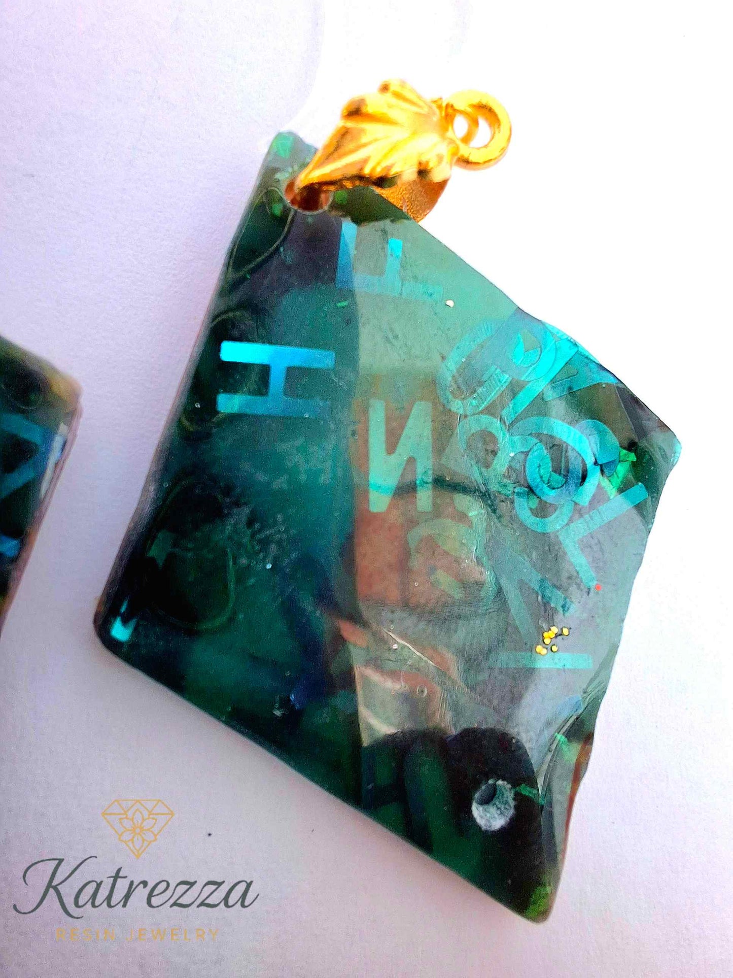 “Green resin earrings with shimmering blue letters and embedded details, geometric double-sided design.”