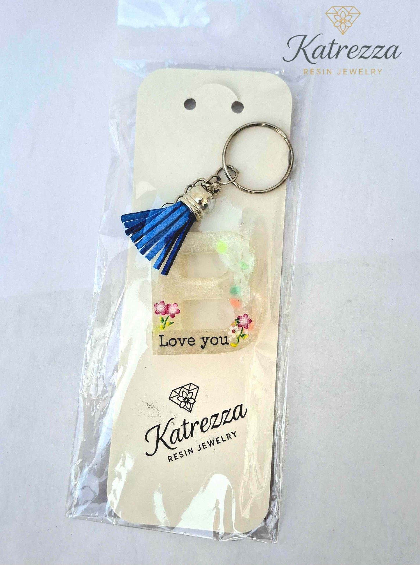 Resin letter B keychain with blue tassel, floral Love You design, glow-in-the-dark, in packaging.