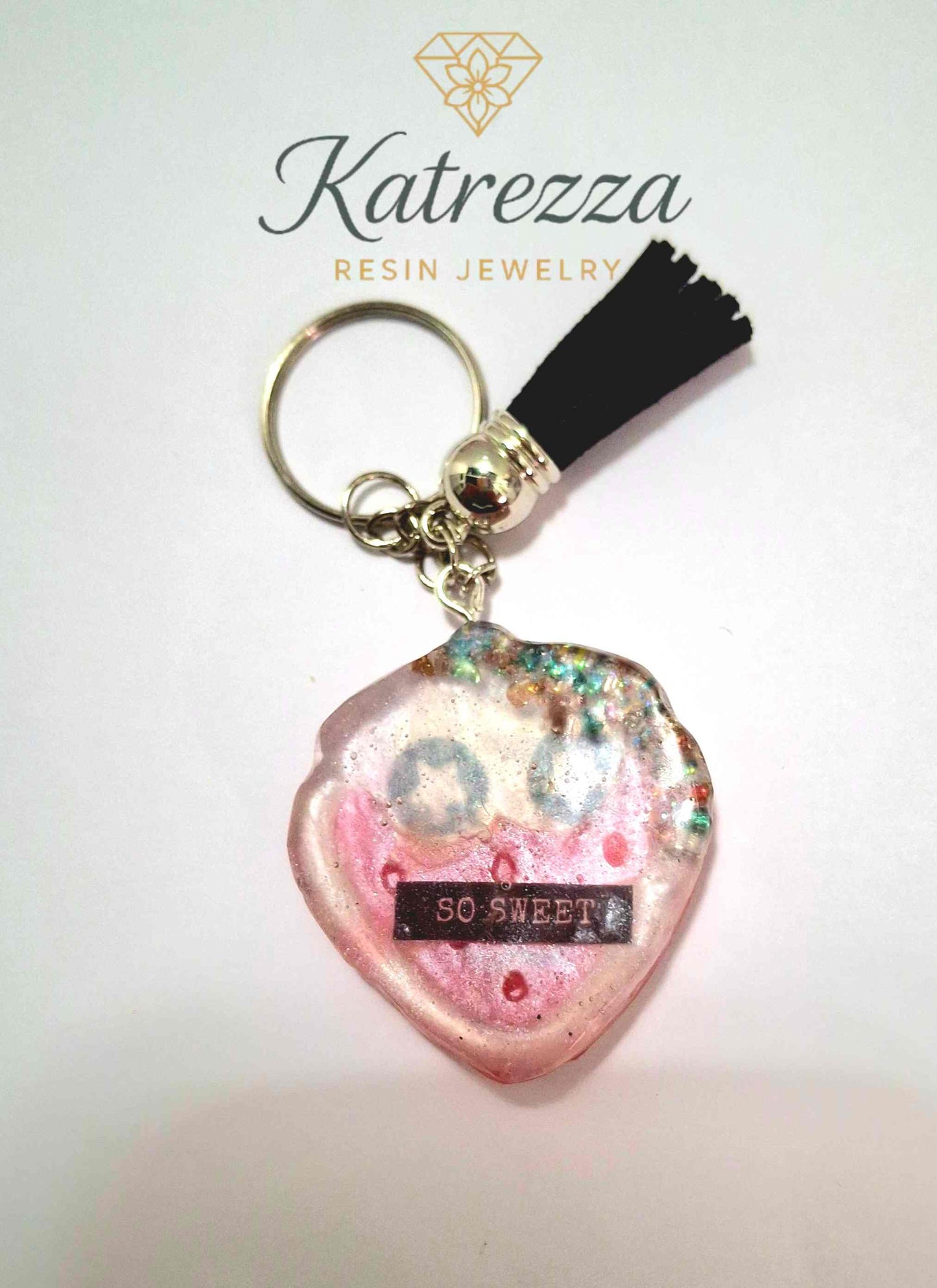 Cute heart-shaped resin keychain with smiling pink face and text “SO SWEET,” part of The Imperfects Collection at Katrezza.