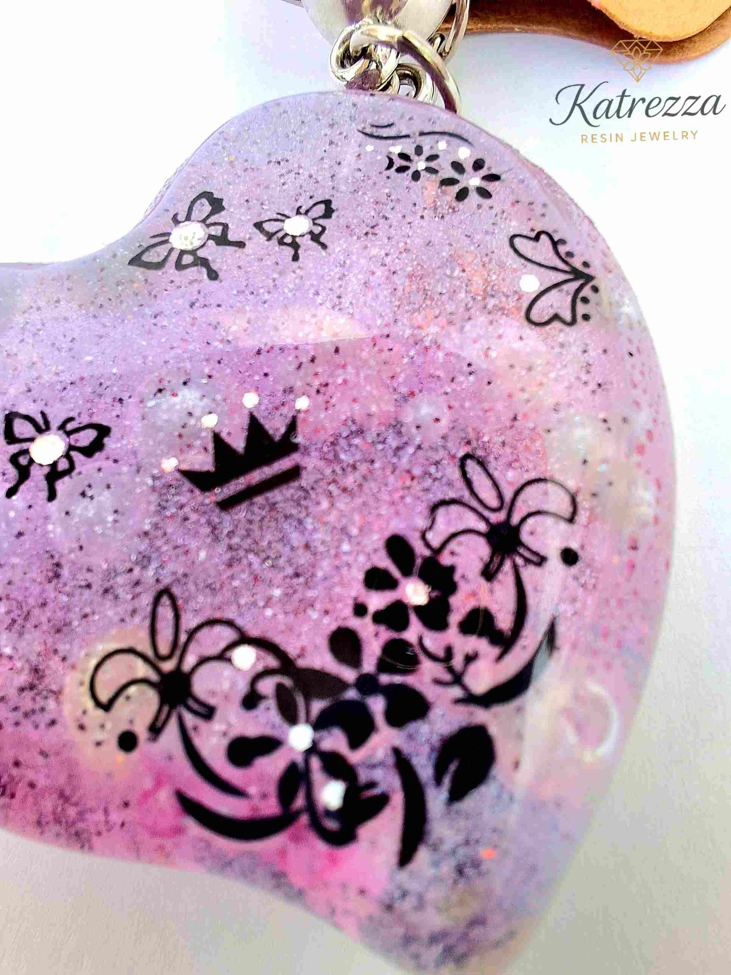 Detailed photo of floral and crown patterns on purple resin heart keychain.
