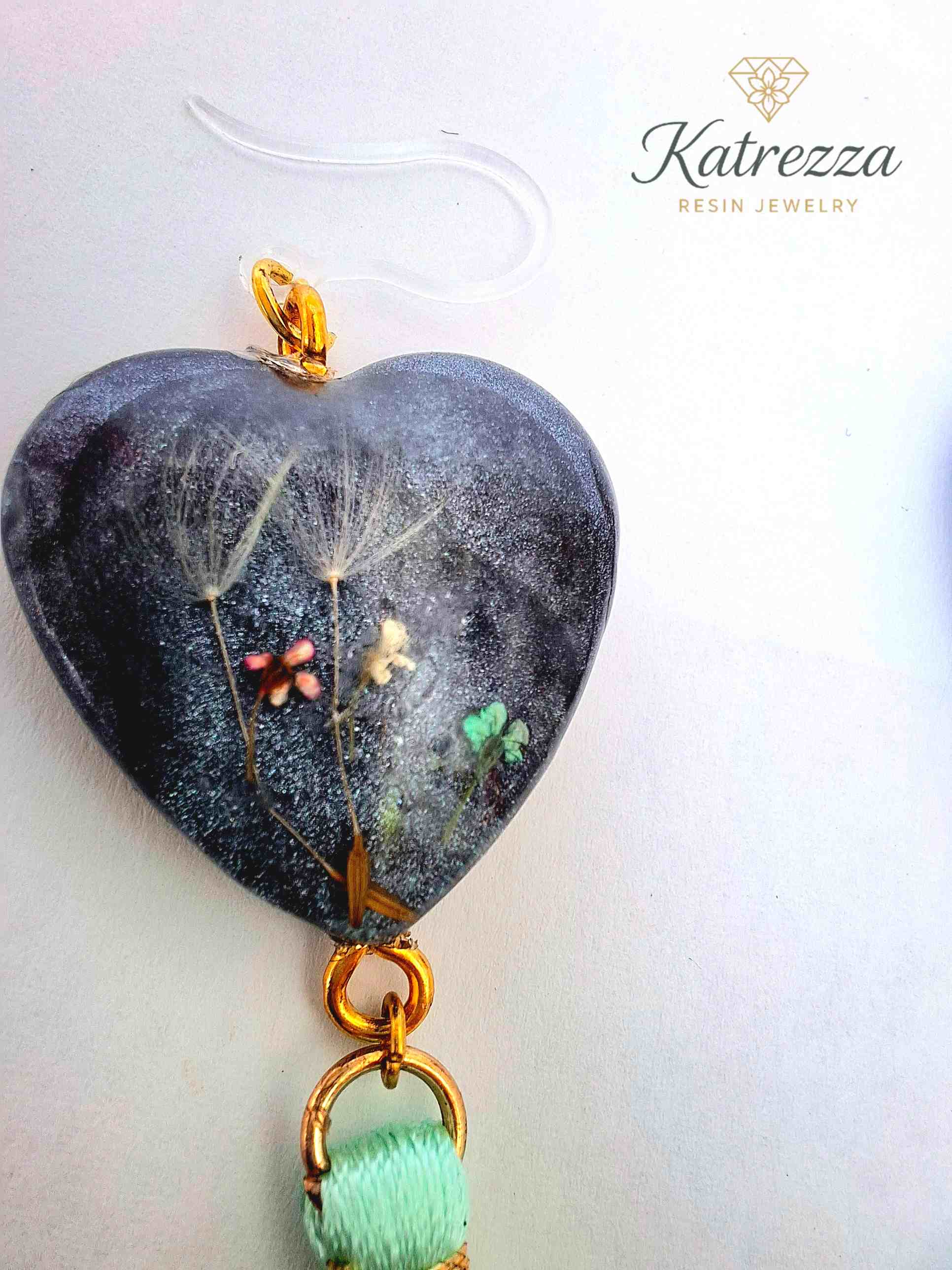 “Close-up of handmade resin earrings with dandelions and tiny flowers preserved inside.”