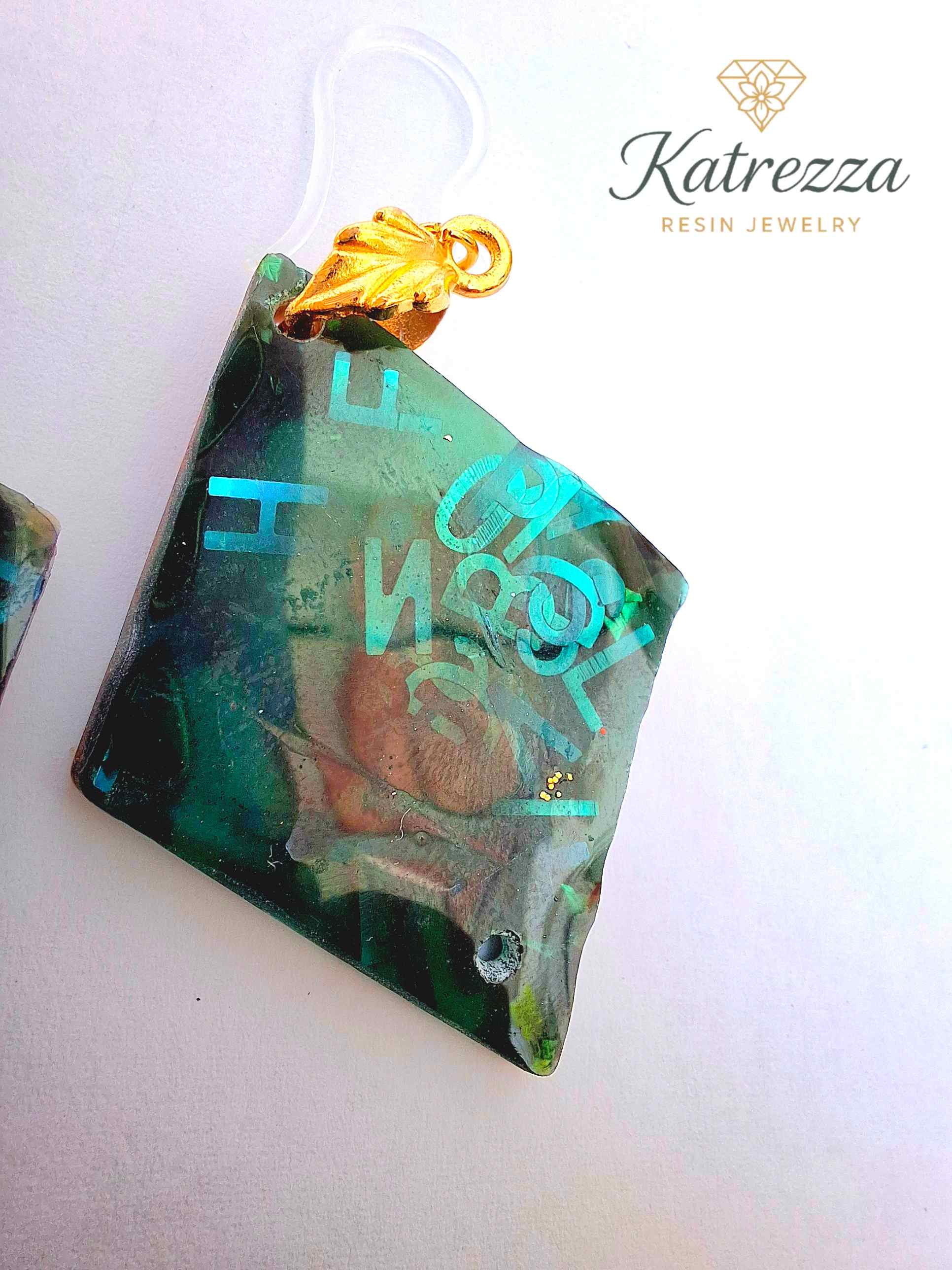 “Green resin earrings with shimmering blue letters and embedded details, geometric double-sided design.”