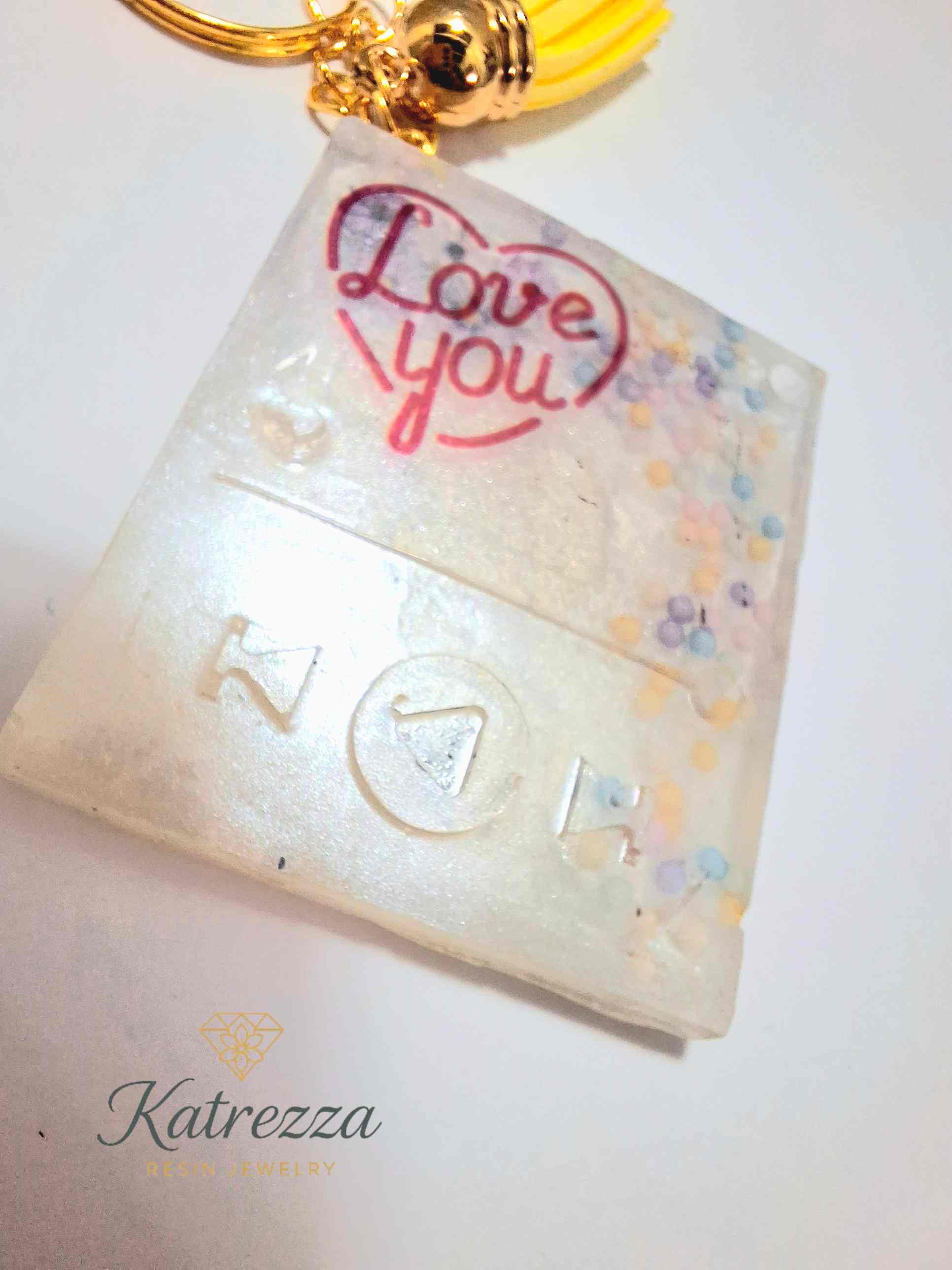 Double-sided handmade resin keychain showing both love messages with yellow tassel.
